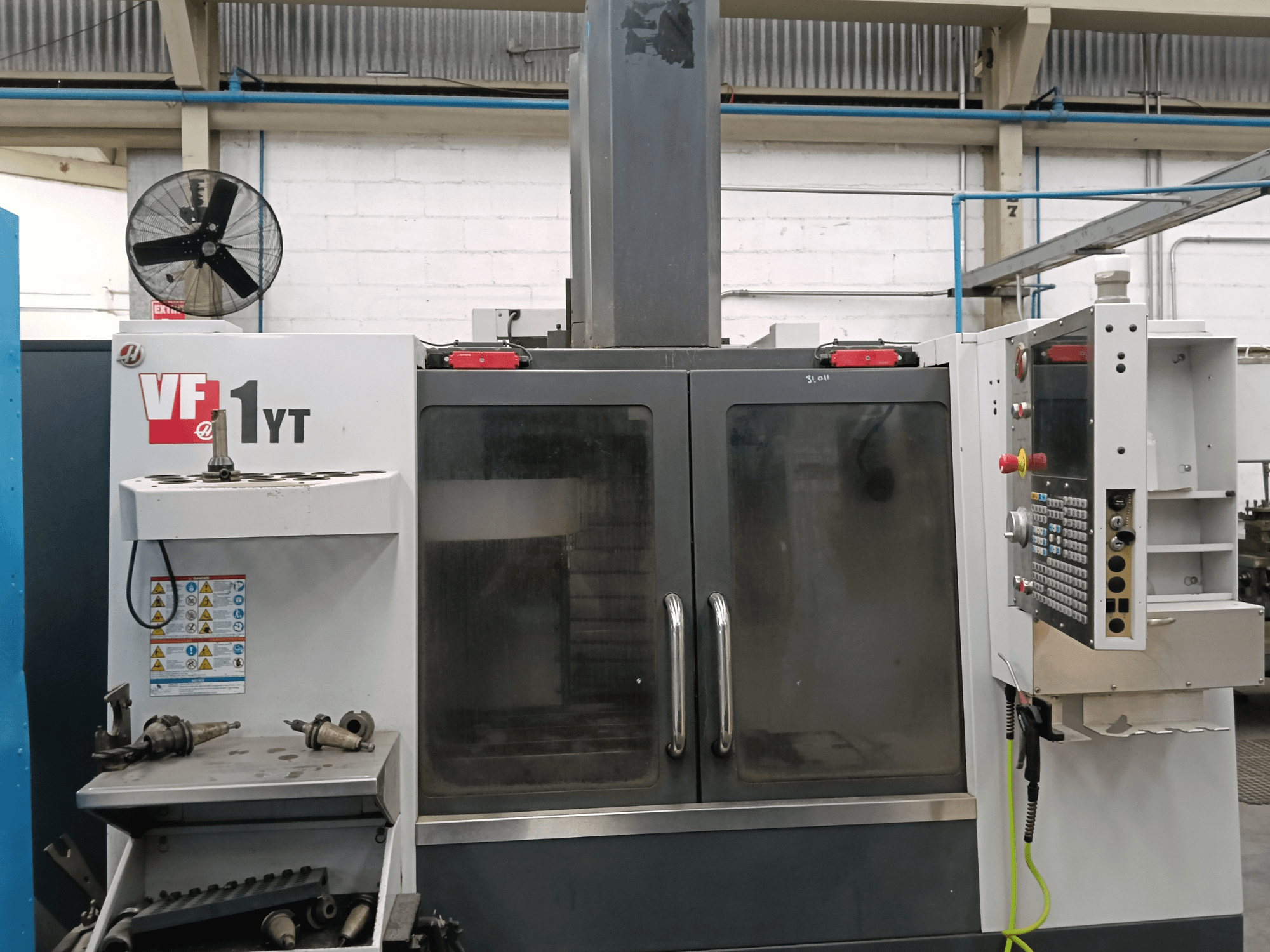 Vista frontale del centro di lavorazione verticale HAAS VF-1YT-1 con pannello di controllo e utensili sul lato.