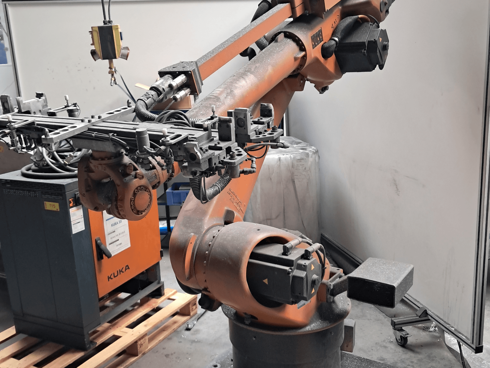 Braccio robotico KUKA KR 30L16-2 visto di profilo, con un effettore terminale complesso e cavi di controllo, affiancato da una centralina KUKA.