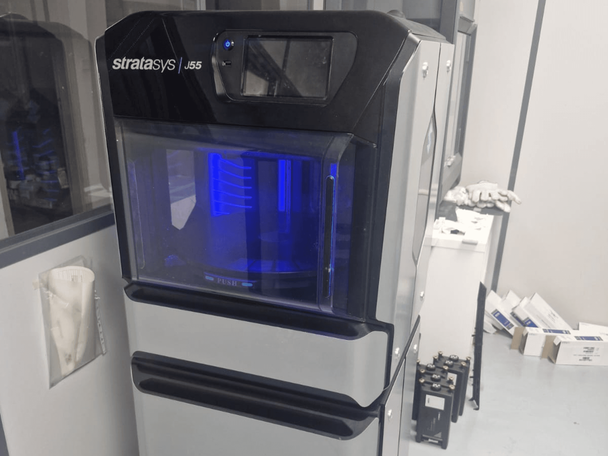 La stampante 3D in plastica Stratasys J55 Prime in una vista laterale, che mostra il suo design elegante e l'area di stampa illuminata.