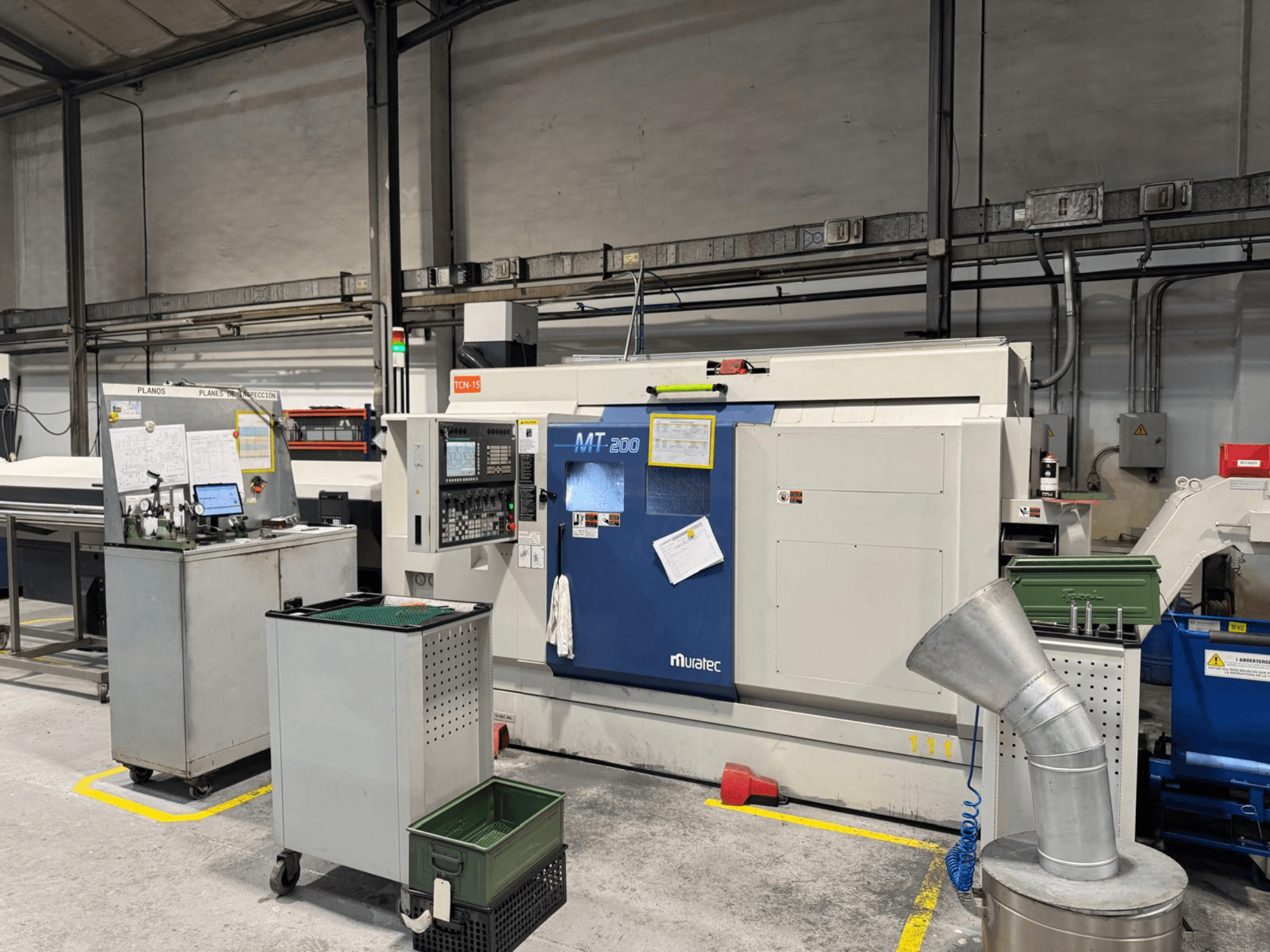 Tornio multimandrino Muratec MT200 in un ambiente di fabbrica, visto dal davanti, con il pannello di controllo e le attrezzature circostanti.