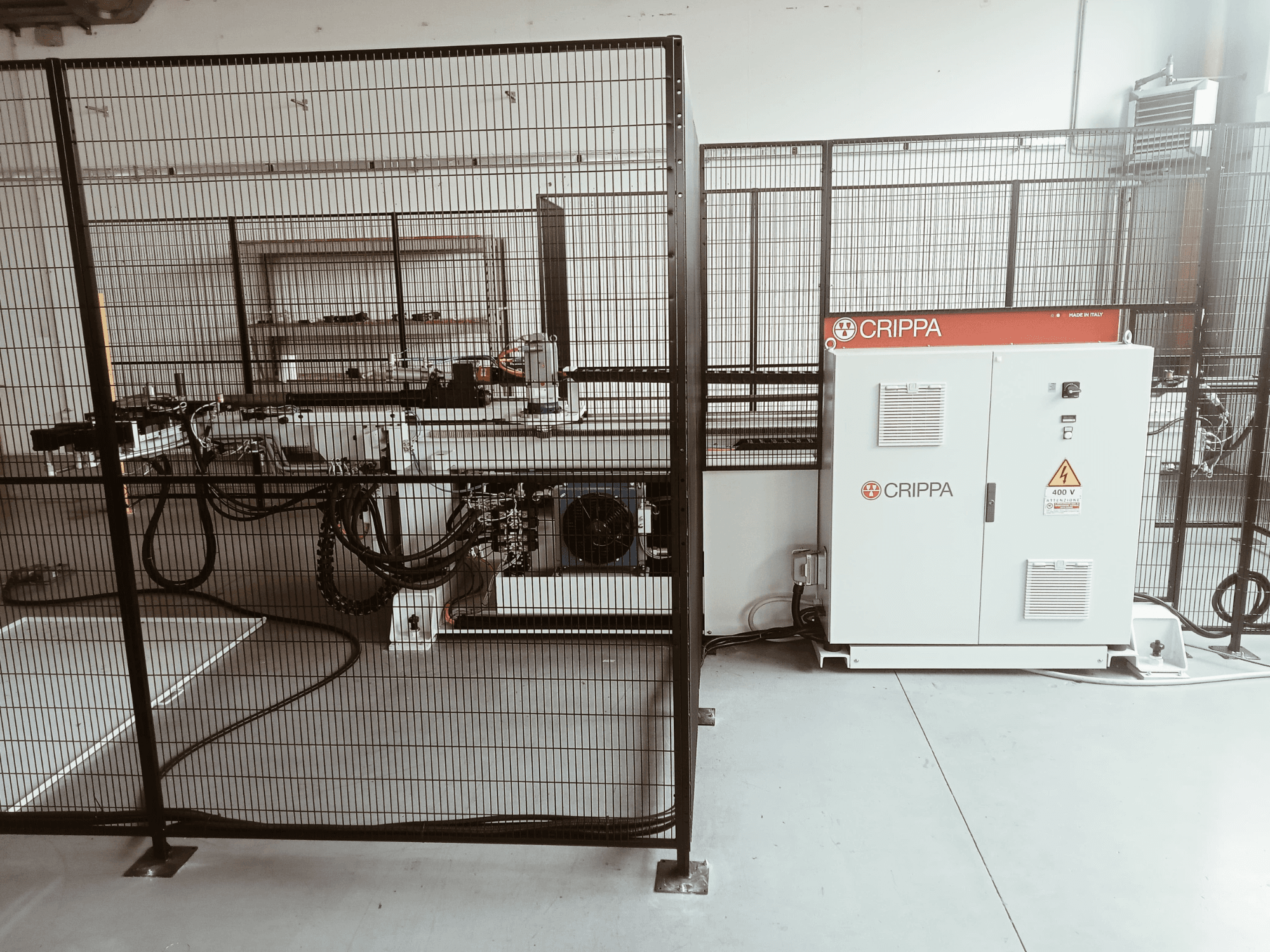 Macchina CRIPPA bianca dietro una gabbia di sicurezza, con tubi e componenti visibili, vista laterale, ambiente industriale.