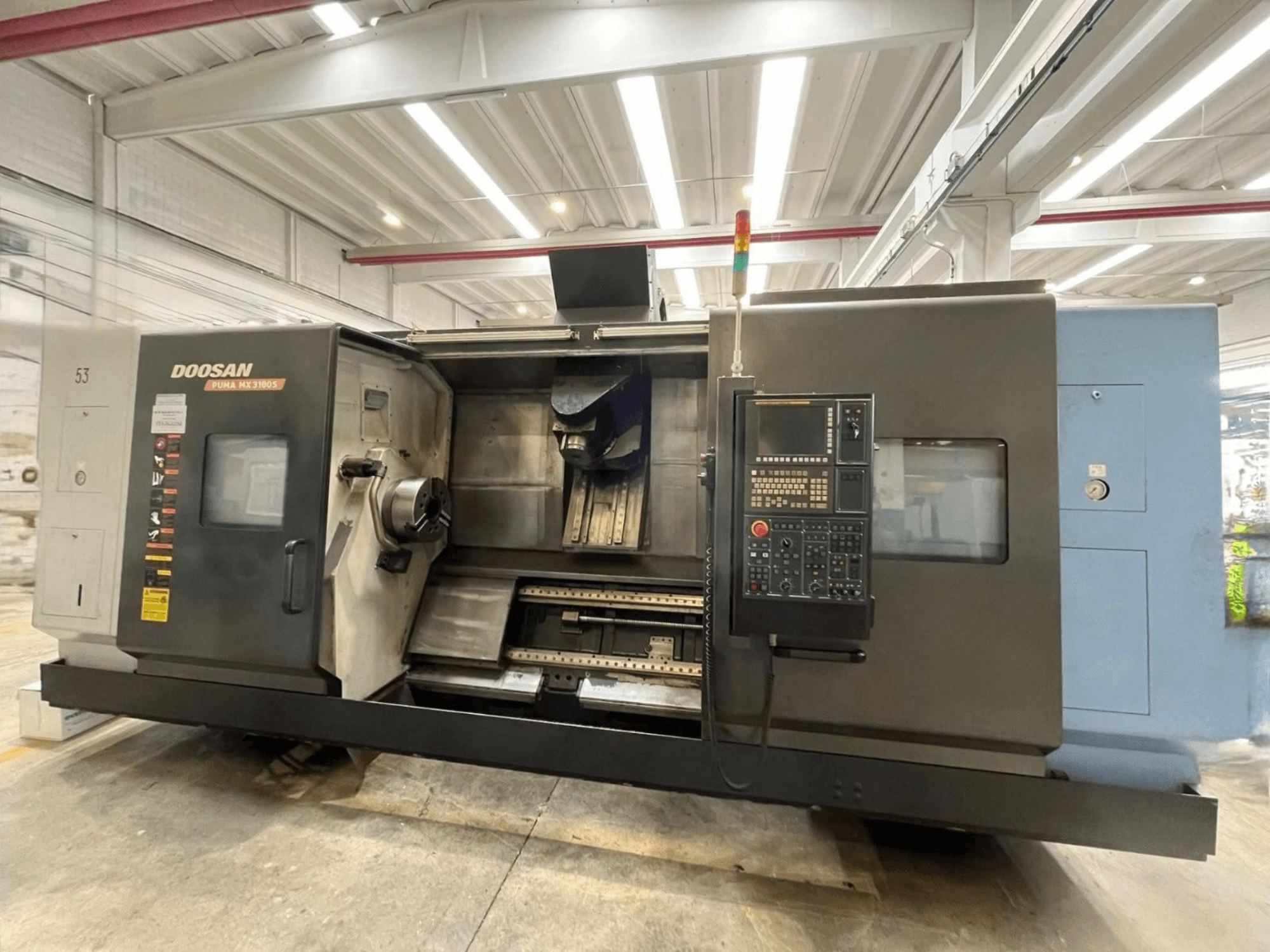 Vista frontale di una tornitrice orizzontale DOOSAN PUMA MX3100 con pannello di comando e zona del mandrino e del portautensili ben visibile.