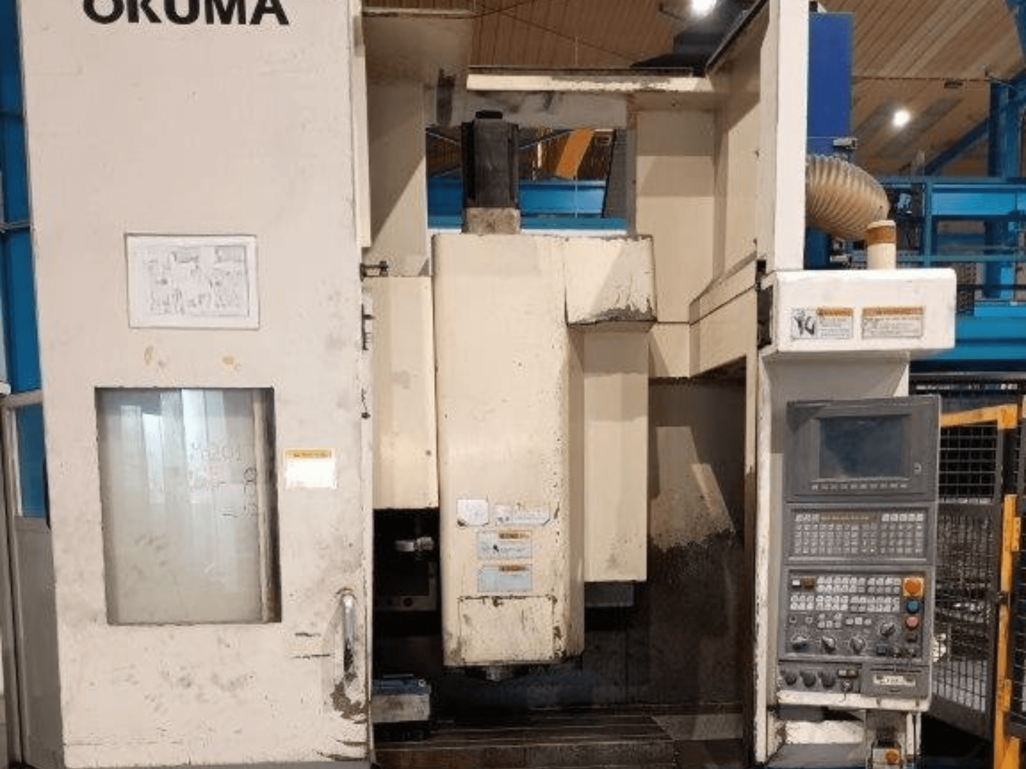 Fresatrice CNC Okuma, vista frontale, con pannello di controllo con pulsanti, display e segni visibili sul corpo macchina.