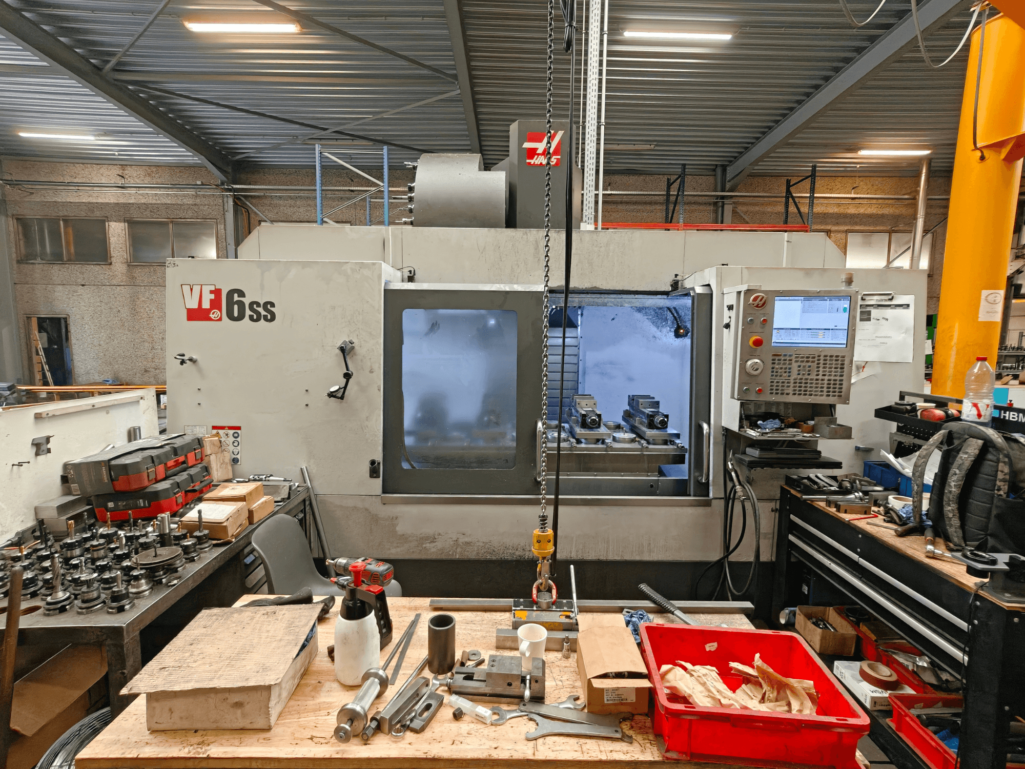 Centro di lavorazione verticale Haas VF-6SS in un'officina; vista laterale che mostra il pannello di controllo e l'area di lavoro ingombra di utensili.