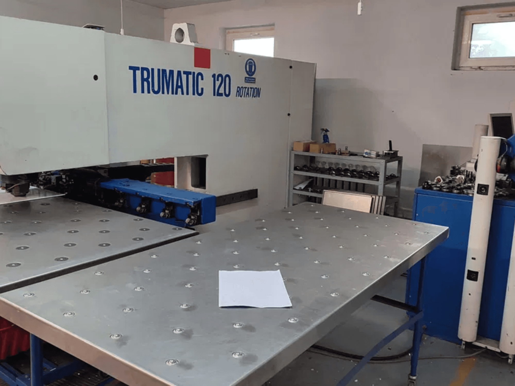 Punzonatrice CNC TRUMPF TRUMATIC 120R vista frontalmente, con tavolo metallico con fori punzonati e foglio bianco.