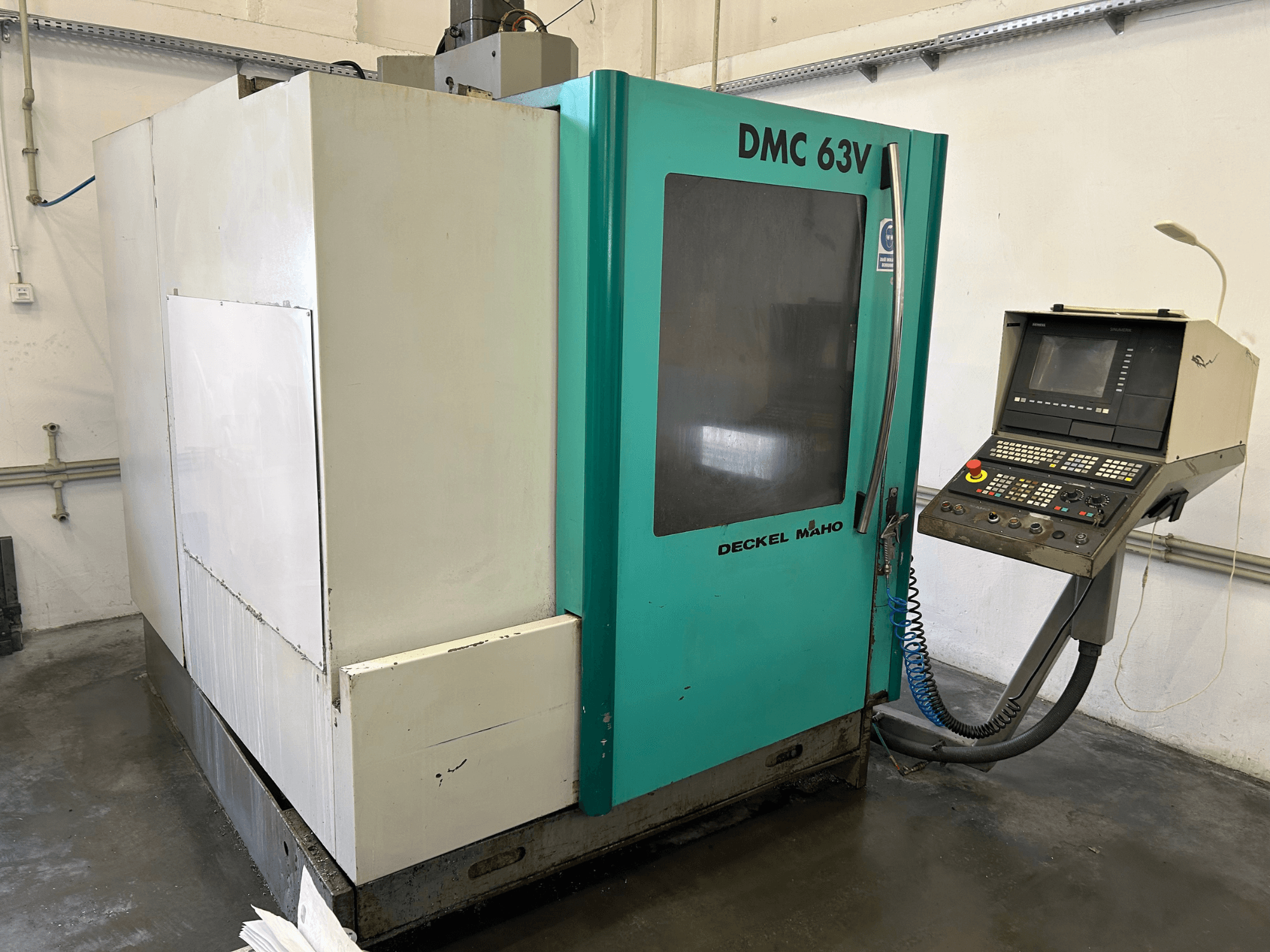 Centro di lavoro verticale DECKEL MAHO DMC 63V in vista frontale, con pannello di controllo e involucro blu-verde.