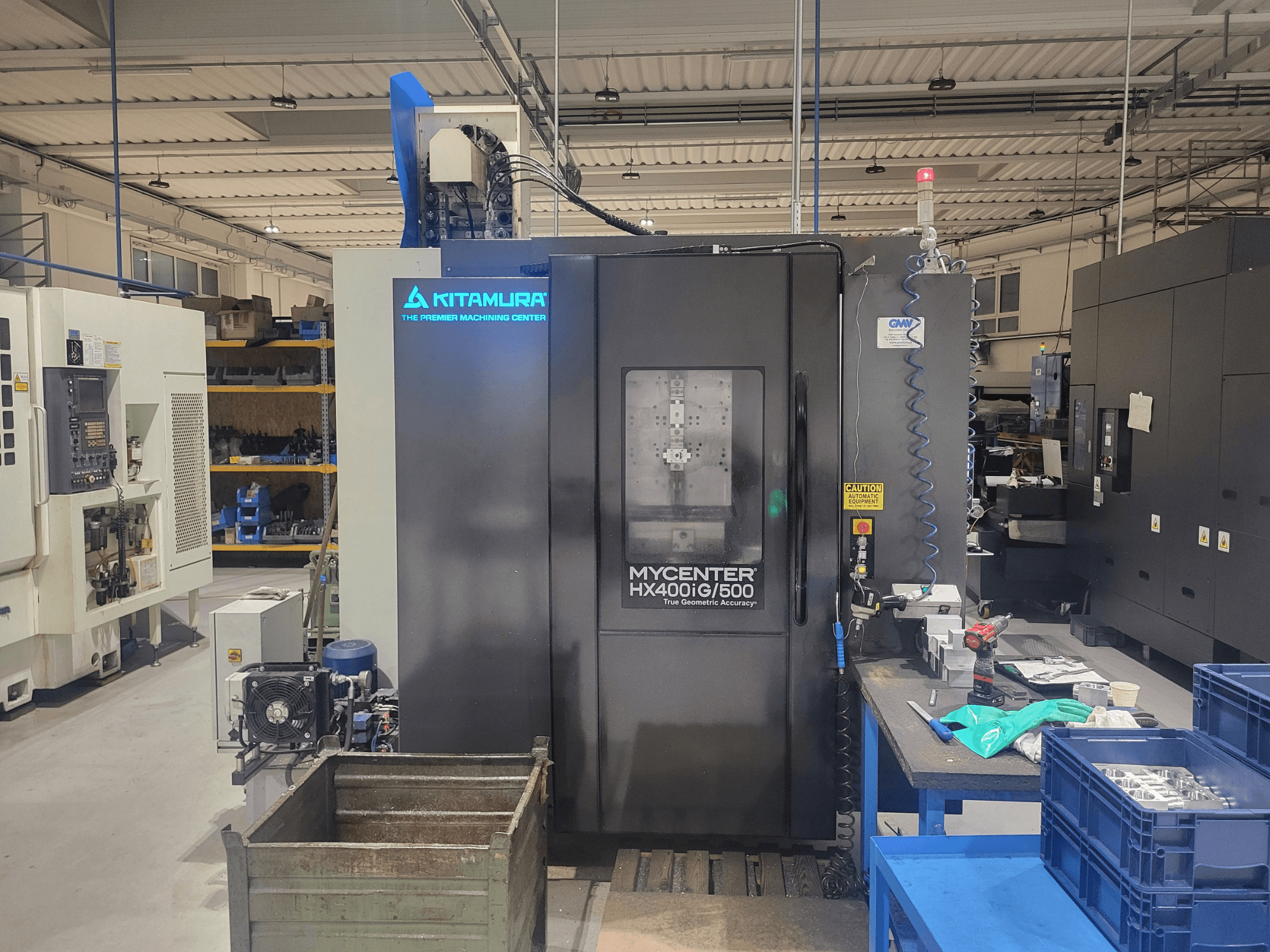 Macchina CNC Kitamura Mycenter HX400iG/500 in un'officina, vista frontale, con comandi, magazzino utensili e materiali nelle vicinanze.