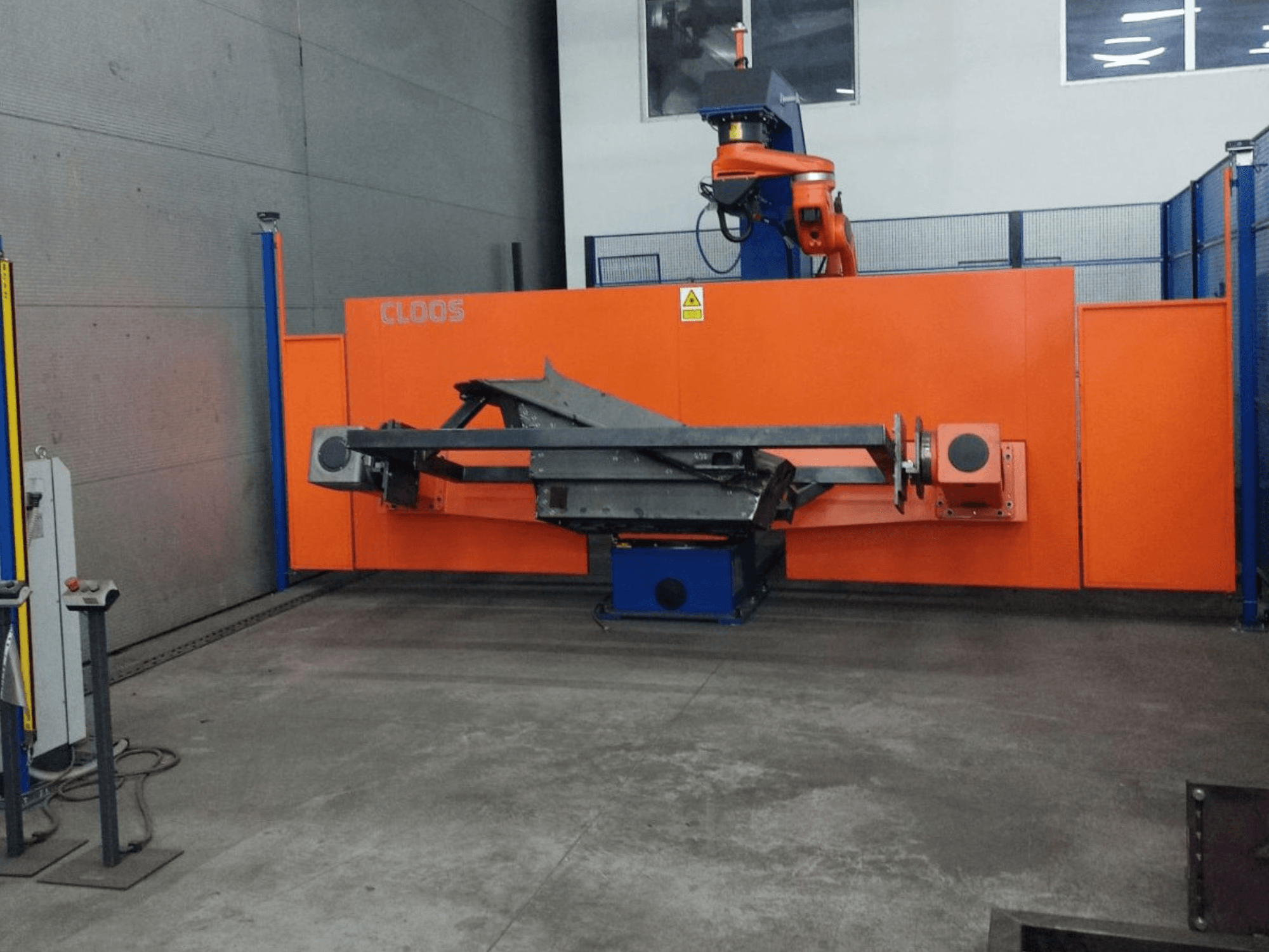 Vista frontale del sistema di automazione CLOOS QIROX QRC-350-E con braccio robotico e struttura metallica in ambiente industriale.