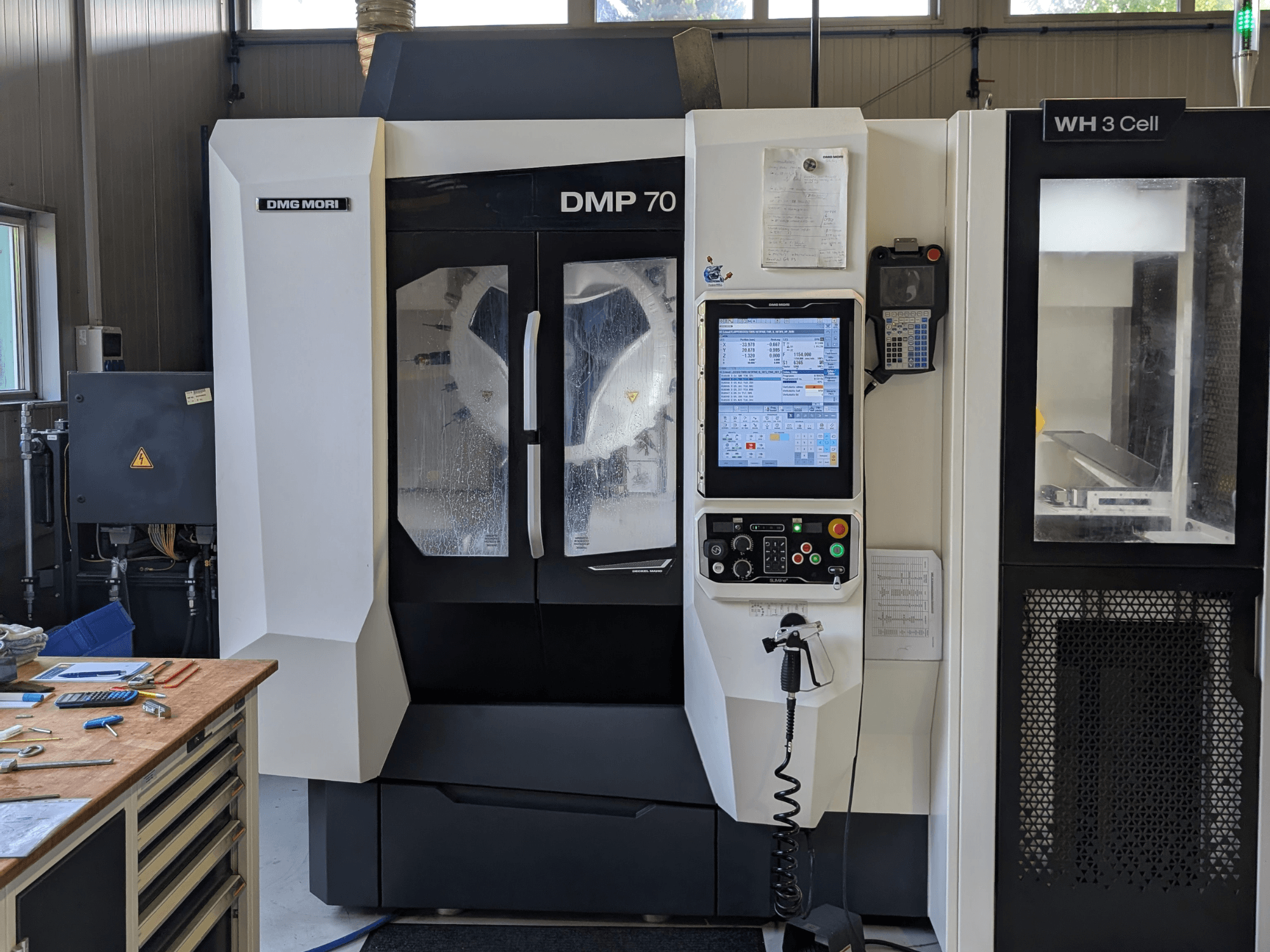 Centro di lavorazione verticale DMG MORI DMP 70, vista frontale con pannello di comando e display operativo, circondato dagli utensili dell'officina.