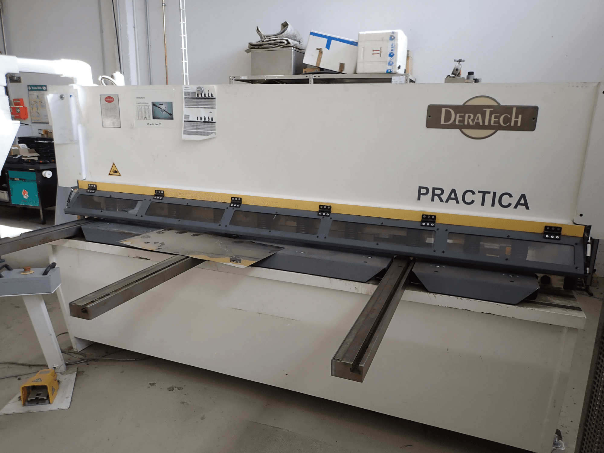 Macchina cesoia DERATECH Practica CNC, vista frontale, che mostra la lama di taglio e le lamiere sul piano di lavoro.