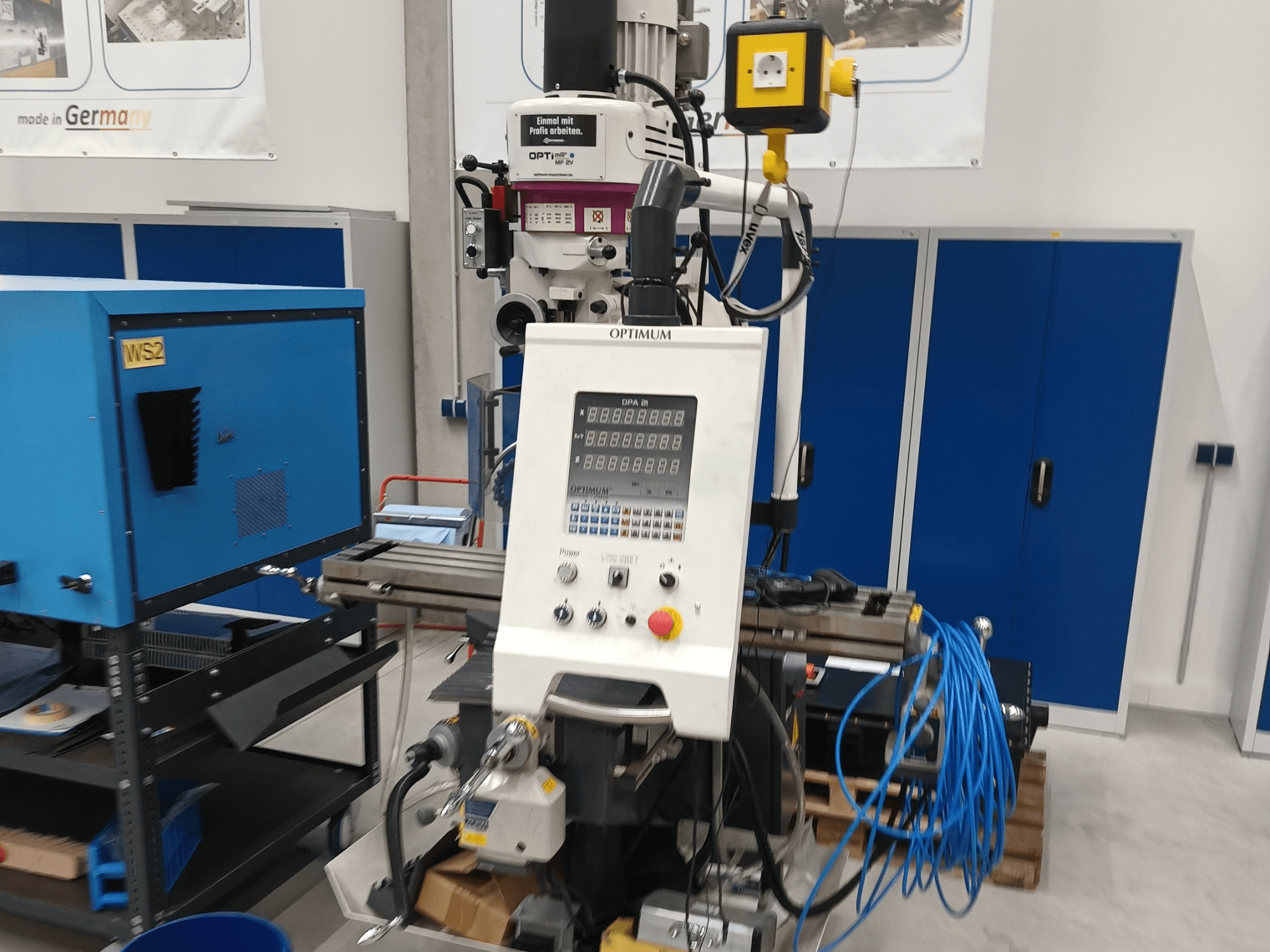 Centro di lavorazione verticale Optimum OPTImill MF 2V, vista frontale che mostra il pannello di controllo, il mandrino e il carrello di supporto blu.