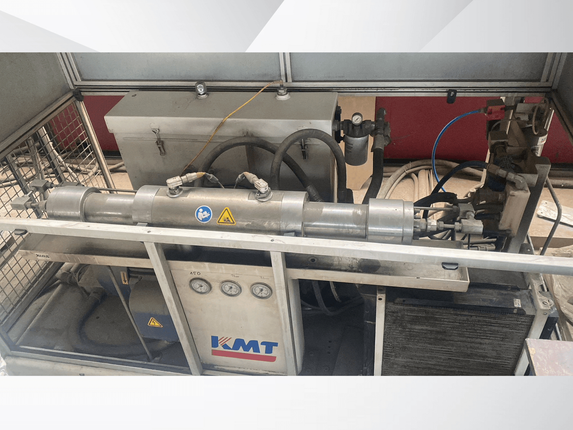 Macchina idraulica KMT in vista frontale, dotata di manometri, tubi e involucro metallico, ideale per applicazioni industriali.