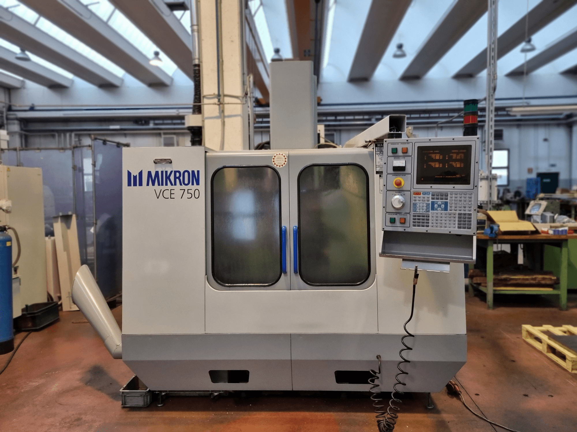 Macchina CNC Mikron VCE 750 bianca in officina, vista laterale, con pannello di controllo digitale e ampie porte in vetro.