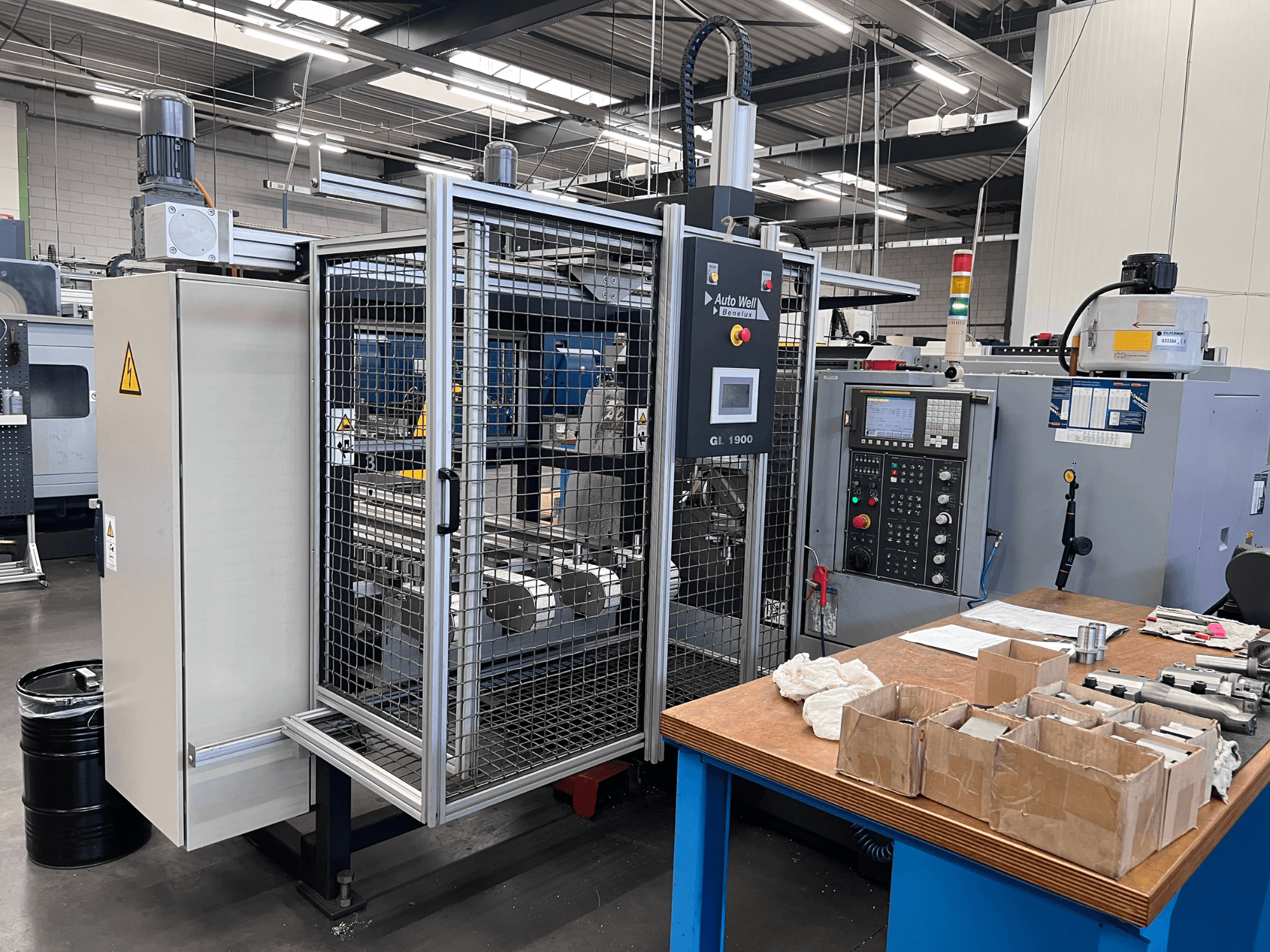 Vista frontale della macchina Auto Weld GL 1900 con il pannello di controllo, la protezione di sicurezza e gli strumenti circostanti su un banco di lavoro.