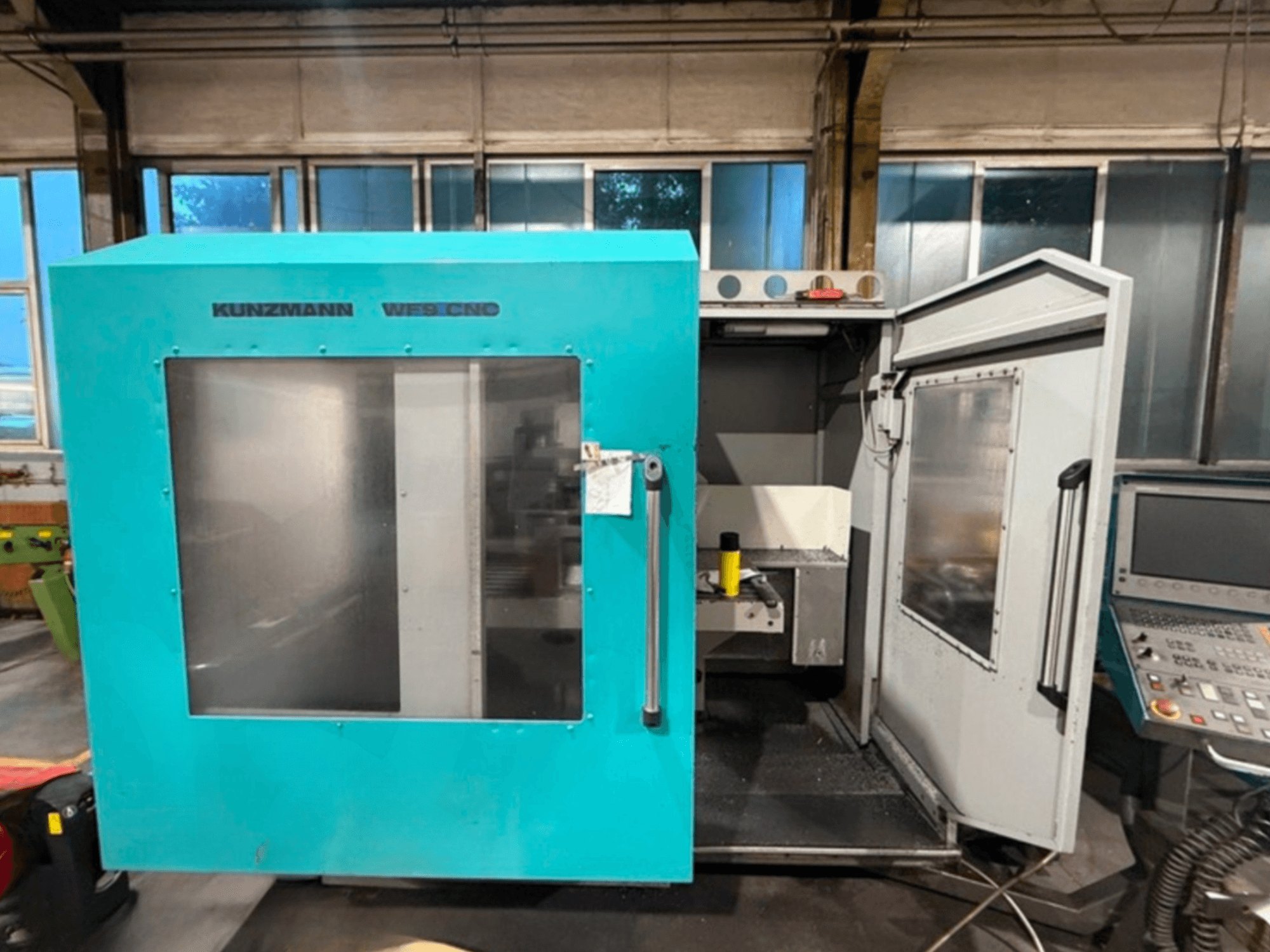 Centro di lavoro verticale CNC KUNZMANN WF9, vista frontale con porte aperte, che mostra l'interno e il pannello di controllo.
