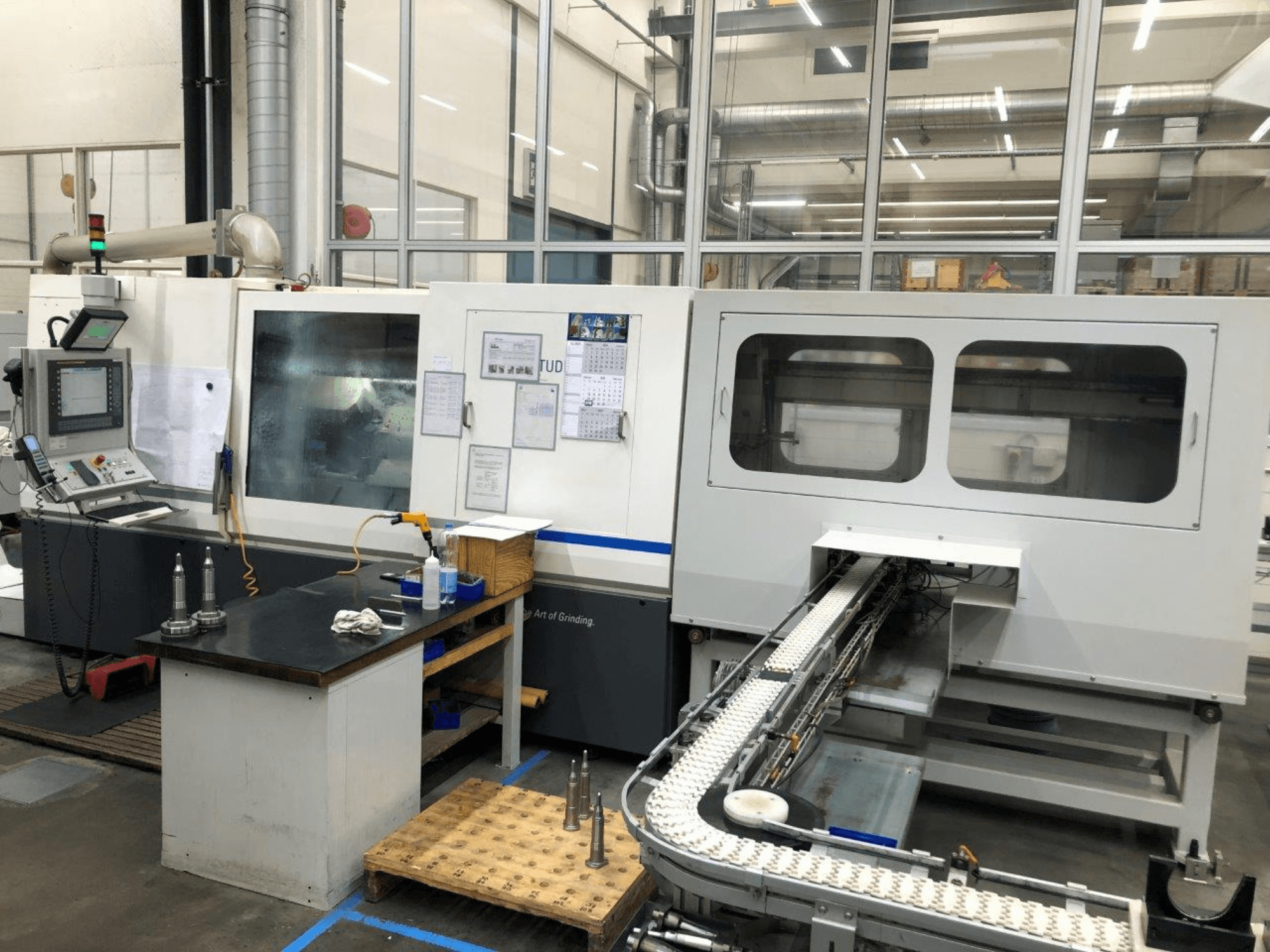 Macchina rettificatrice CNC con pannello di controllo, vista frontale; presenta un convogliatore e finestre di visualizzazione chiare, che mettono in mostra gli utensili di precisione.