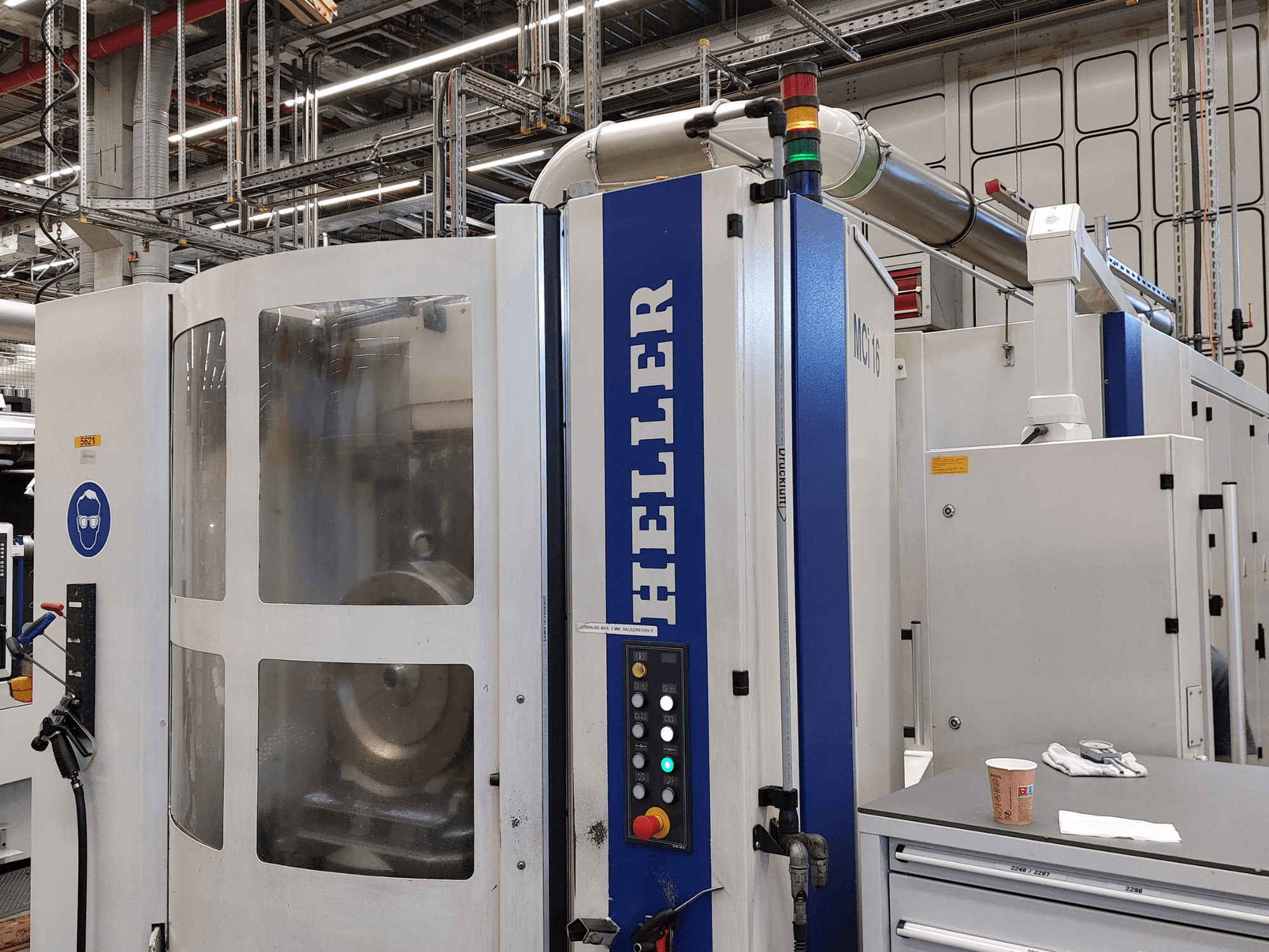 Centro di lavorazione verticale Heller MCI 16 in un ambiente industriale, con pannello di controllo e segnaletica di sicurezza.