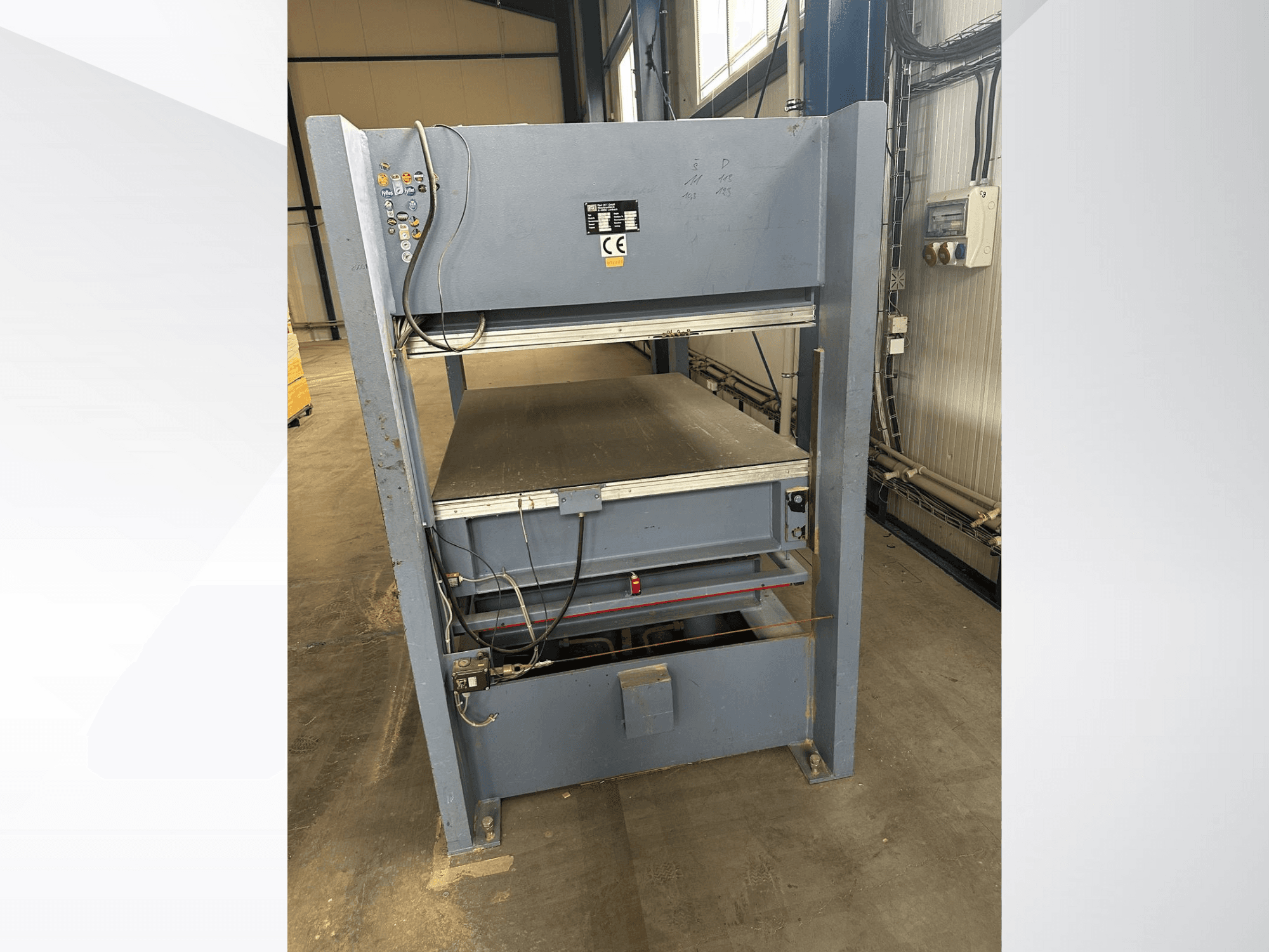 Macchina industriale grigia con pannello di controllo, vista dal davanti; include piattaforme regolabili e marcature di sicurezza.