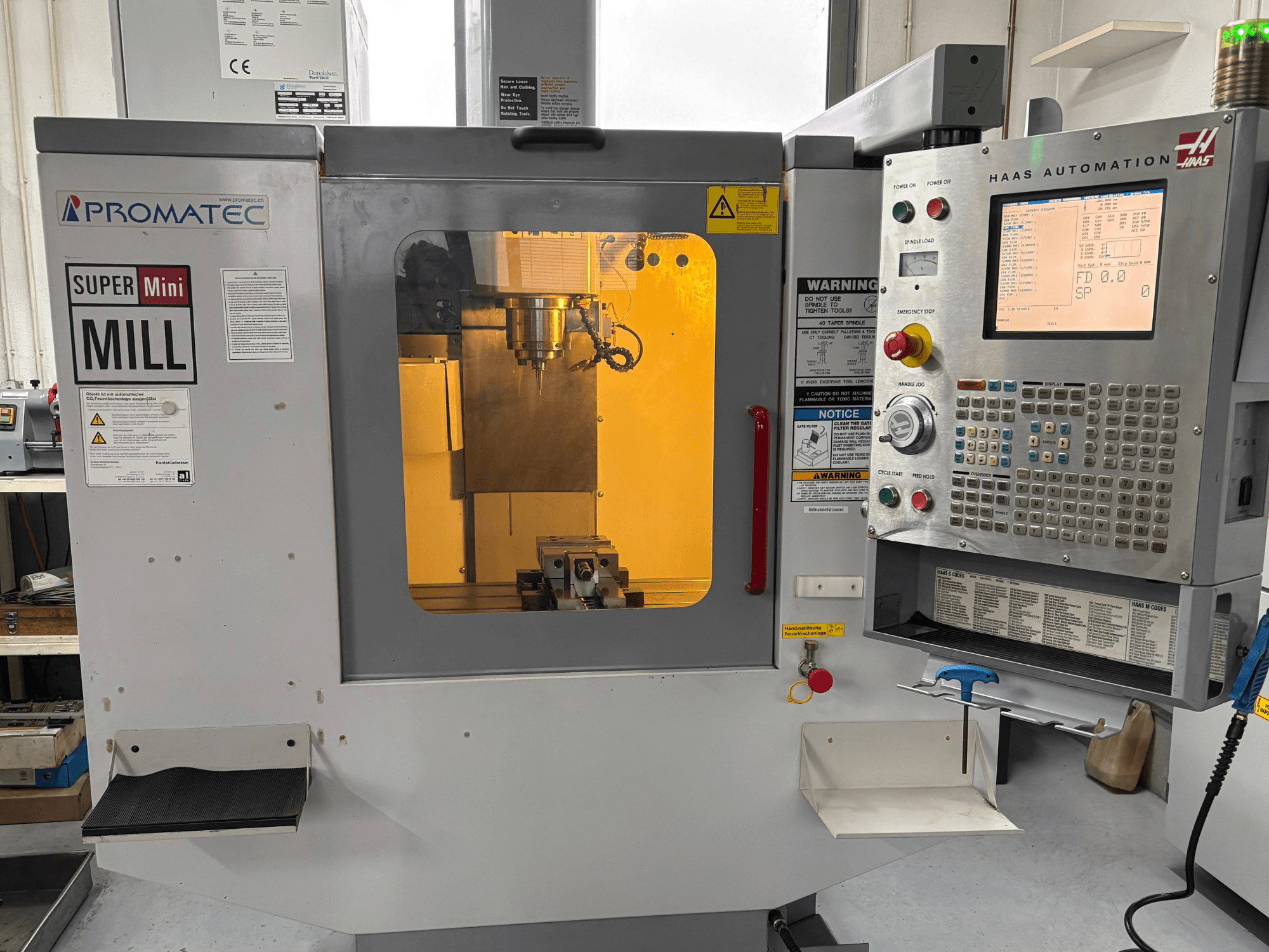 Promatec Super Mini Mill in vista frontale, dotato di un pannello di controllo Haas Automation e di un utensile di taglio visibile all'interno.