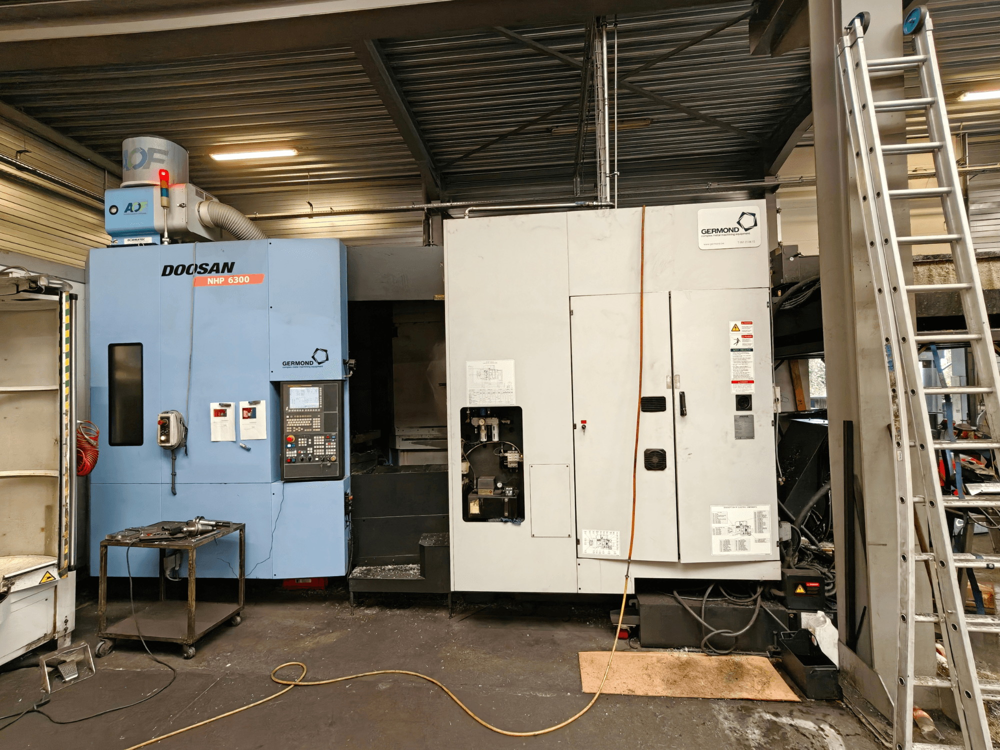 Centro di lavorazione orizzontale DOOSAN NHP6300 visto frontalmente, con in primo piano il pannello di controllo e le macchine adiacenti in un ambiente di officina.