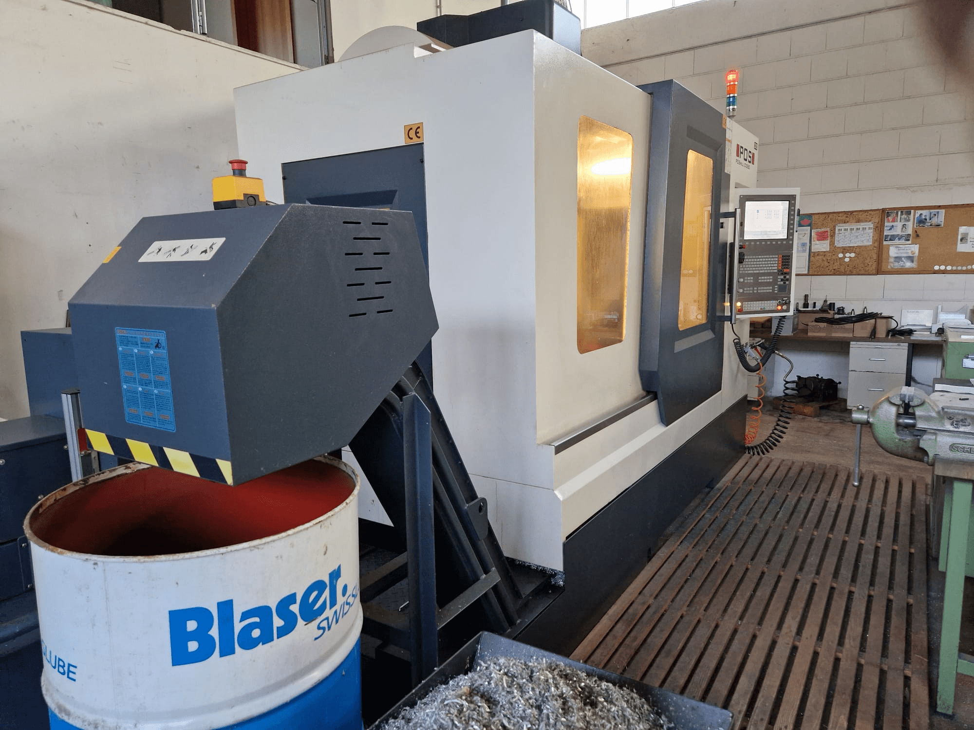 Vista frontale del centro di lavoro verticale POSmill C 1050, con sistema di raffreddamento sopra il tamburo Blaser e pannello di controllo visibile.