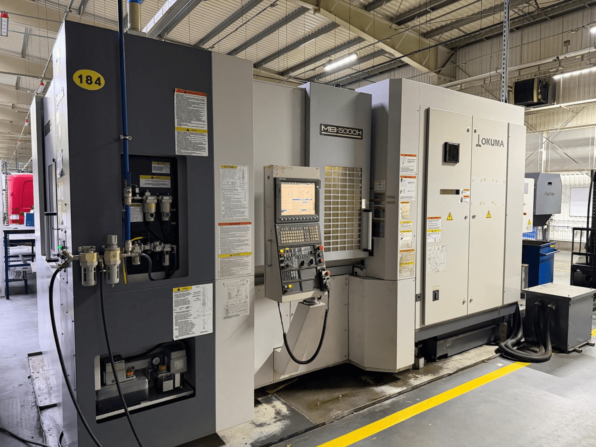 Centro di lavoro orizzontale Okuma MB 5000H vista frontale, con comandi, etichettatura e collegamenti idraulici.