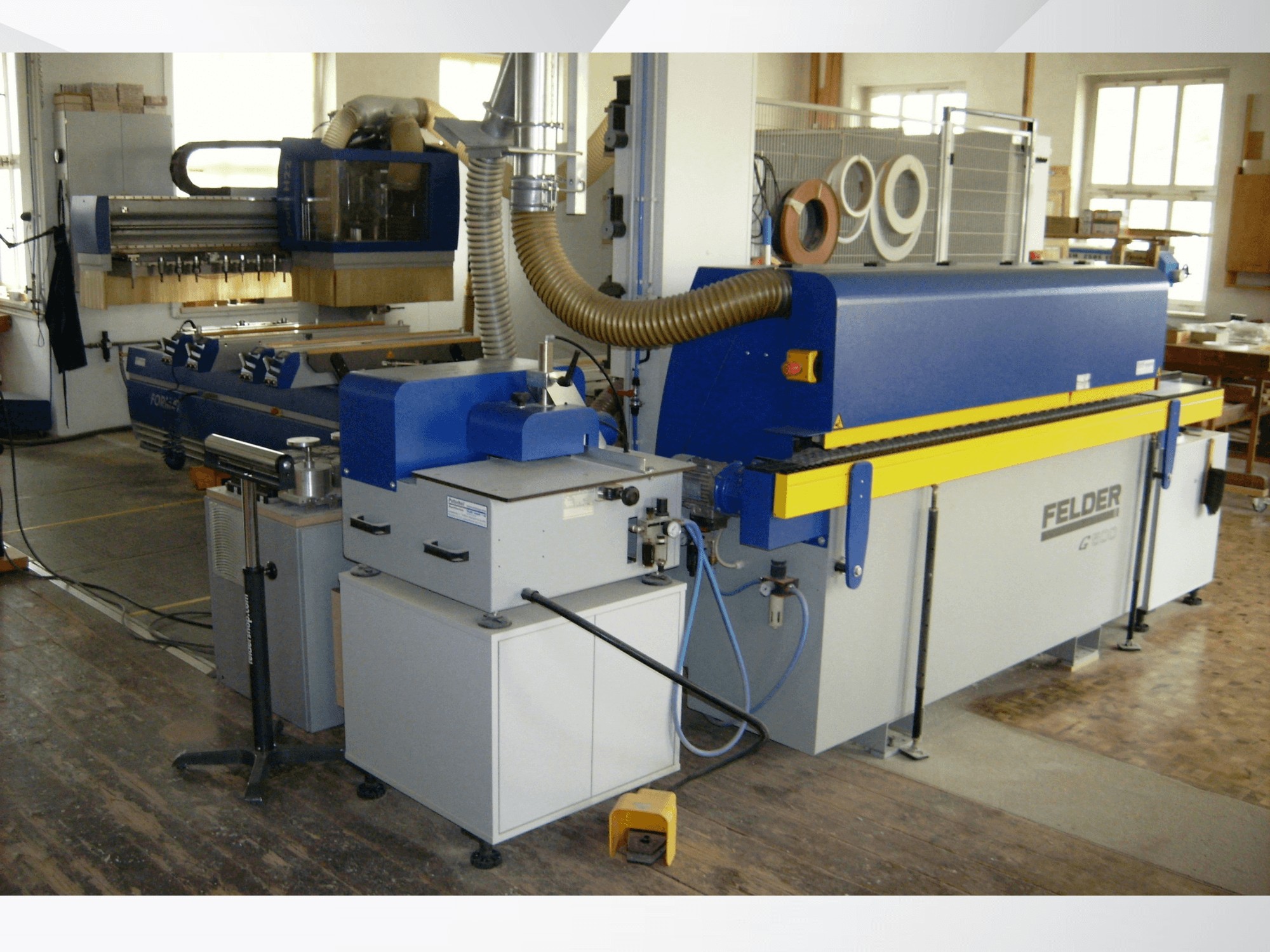 Bordatrice FELDER G500 in un'officina, vista laterale che mostra la struttura blu e gialla con i comandi e i condotti.