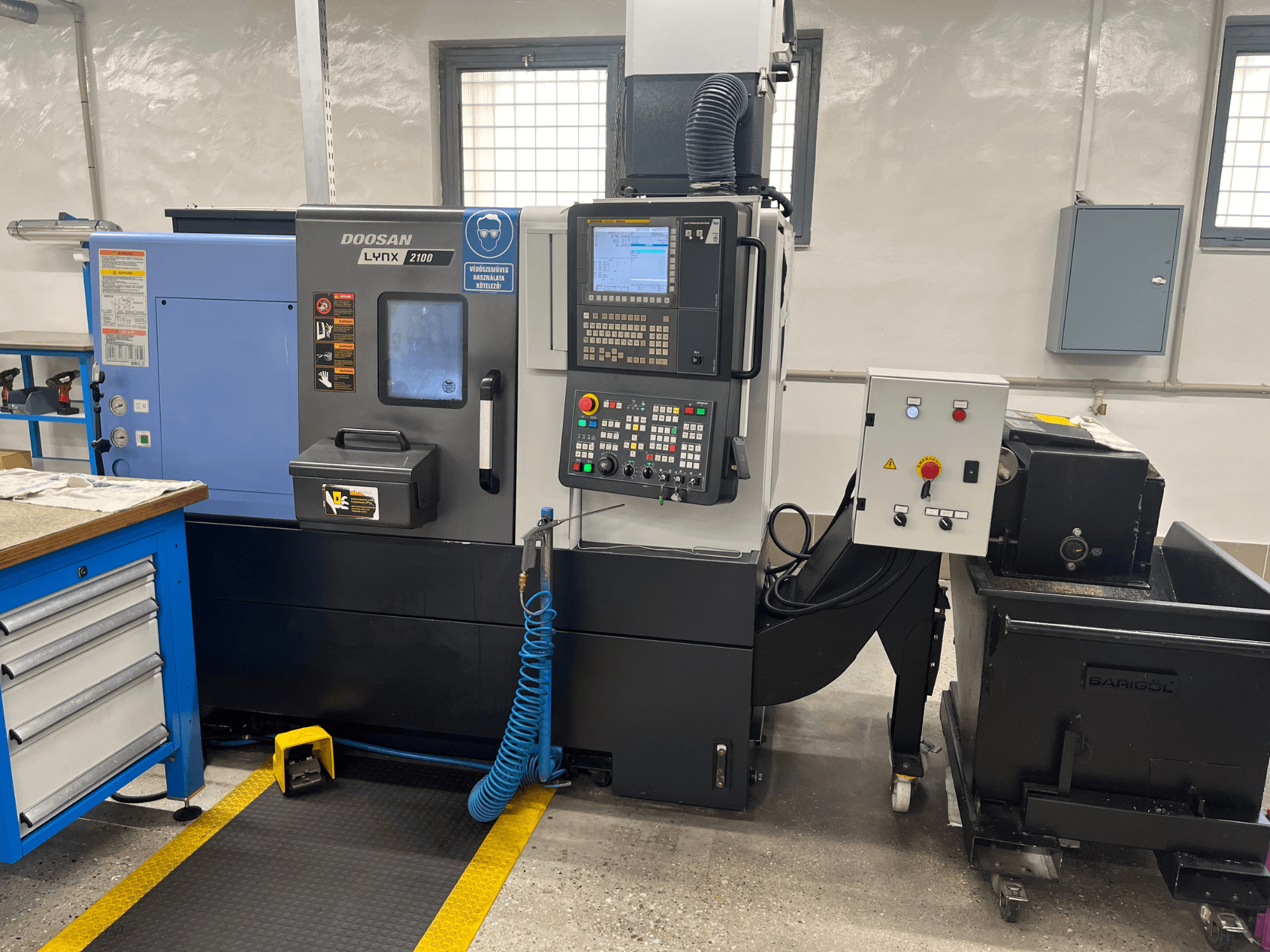 Tornio Doosan Lynx 210 in officina, con pannello di controllo, magazzino utensili e sistema di raffreddamento, vista laterale con dettagli dello spazio di lavoro.