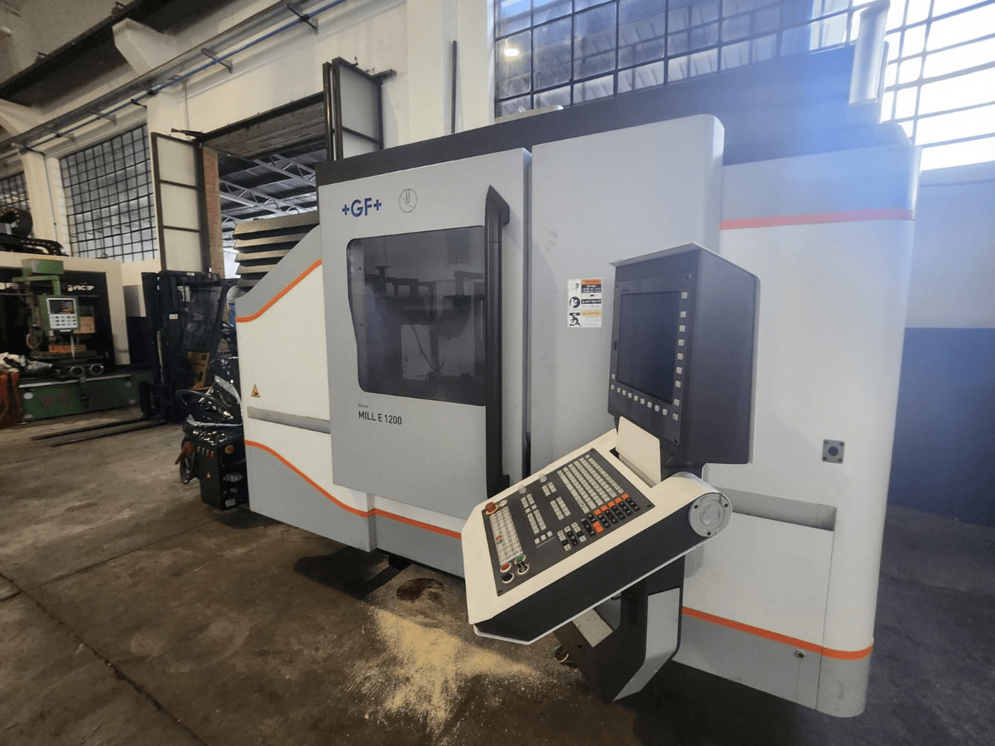 GF MILL E1200, vista frontale della fresatrice con pannello di controllo, display ed etichette di sicurezza, in un'officina.