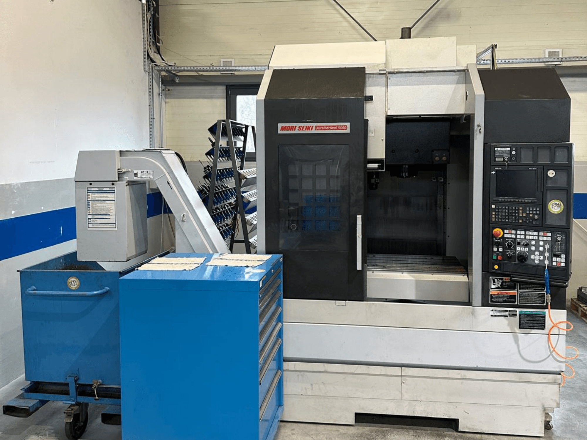 MORI SEIKI DURA VERTICAL 5060, vista frontale di un centro di lavorazione verticale con pannello di controllo e magazzino utensili adiacente.