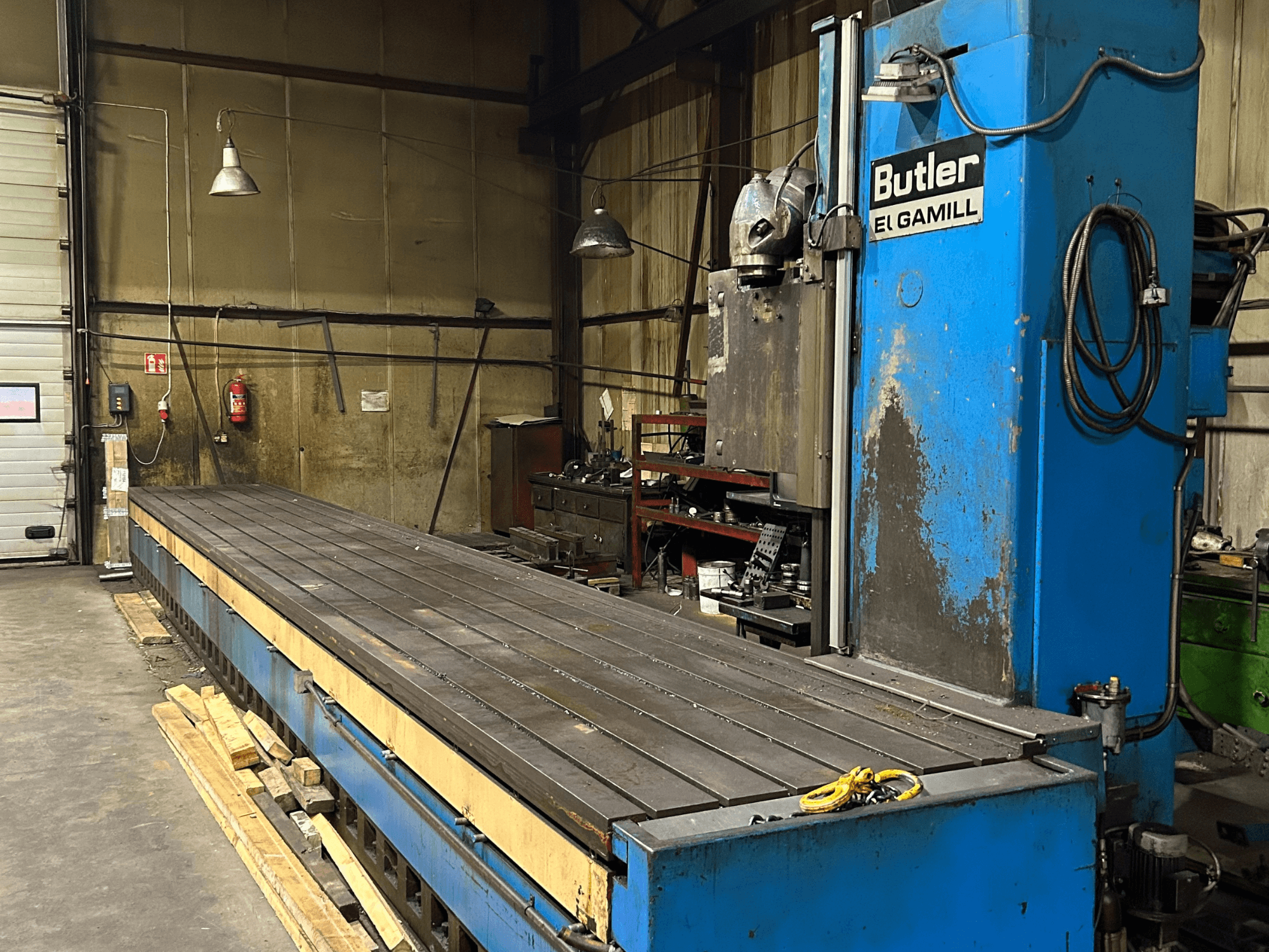 Fresatrice Butler El Gamill blu in un'officina, vista laterale che mostra un lungo tavolo piatto e i comandi sulla destra.