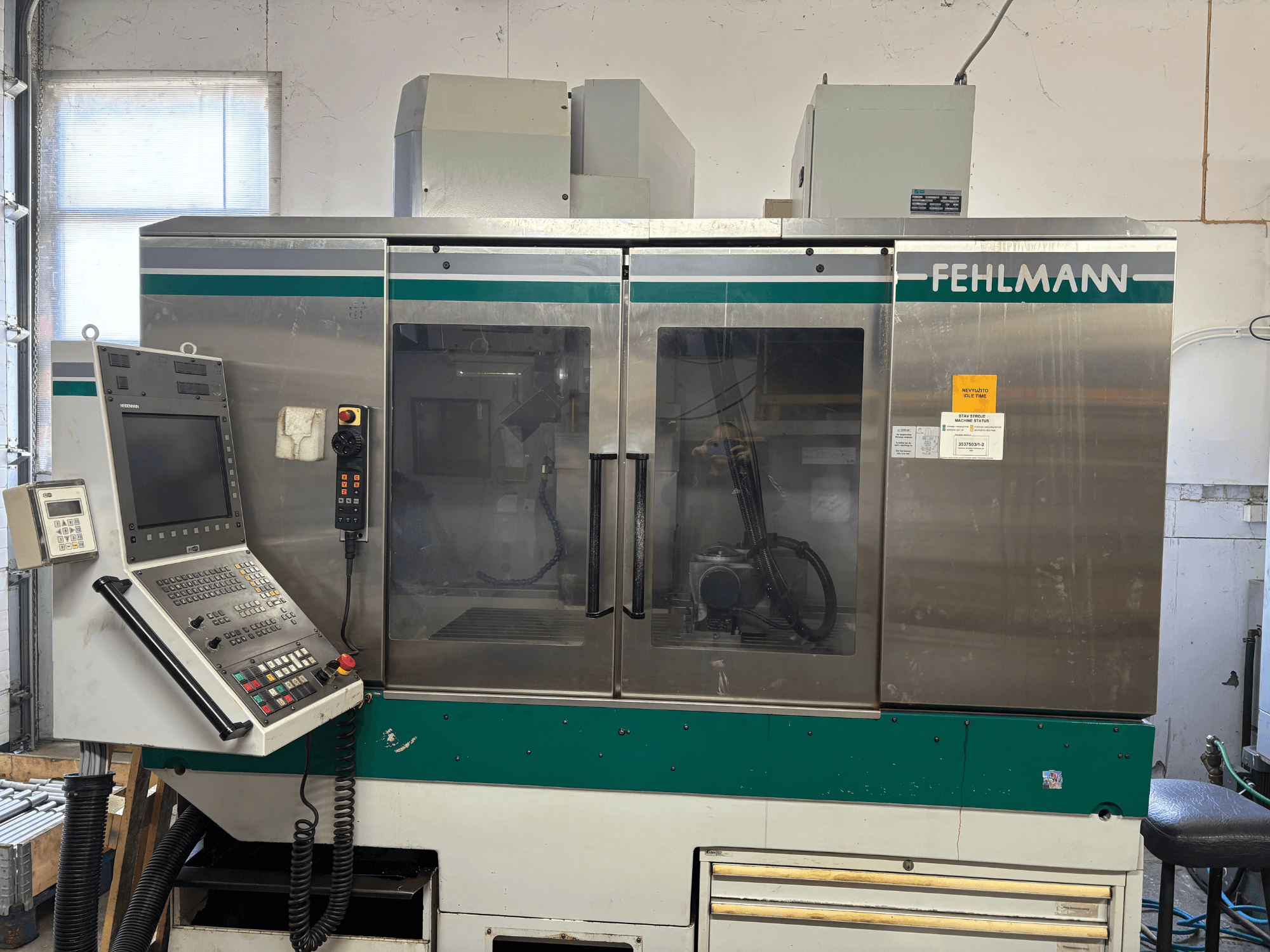 Vista frontale del centro di lavorazione verticale FEHLMANN Picomax 90-M, con pannello di controllo, carenatura trasparente e pulsanti di comando.