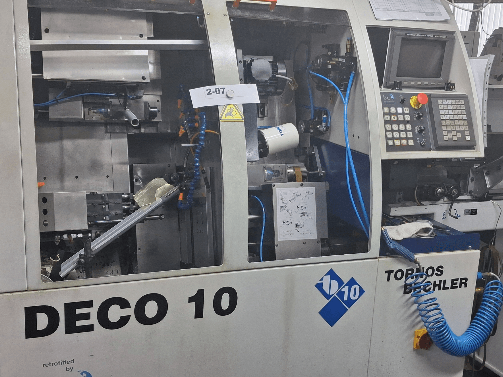 Vista ravvicinata del tornio TORNOS Deco 10a di tipo svizzero, che mostra i dettagli del meccanismo interno e del pannello di controllo.