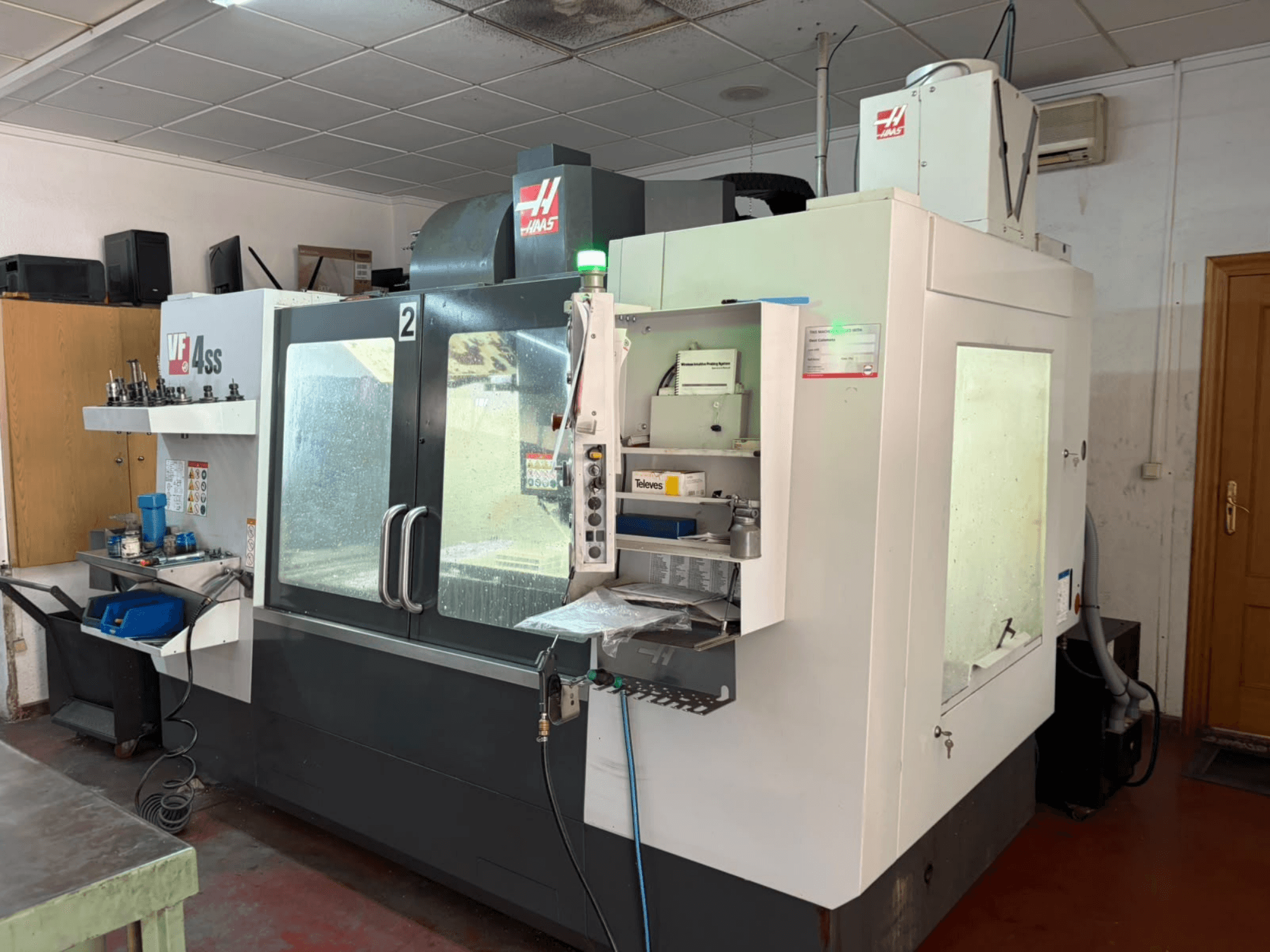 Centro di lavorazione verticale HAAS VF 4SS in un'officina, vista frontale, con il pannello di controllo e l'area di lavoro con utensili e materiali.