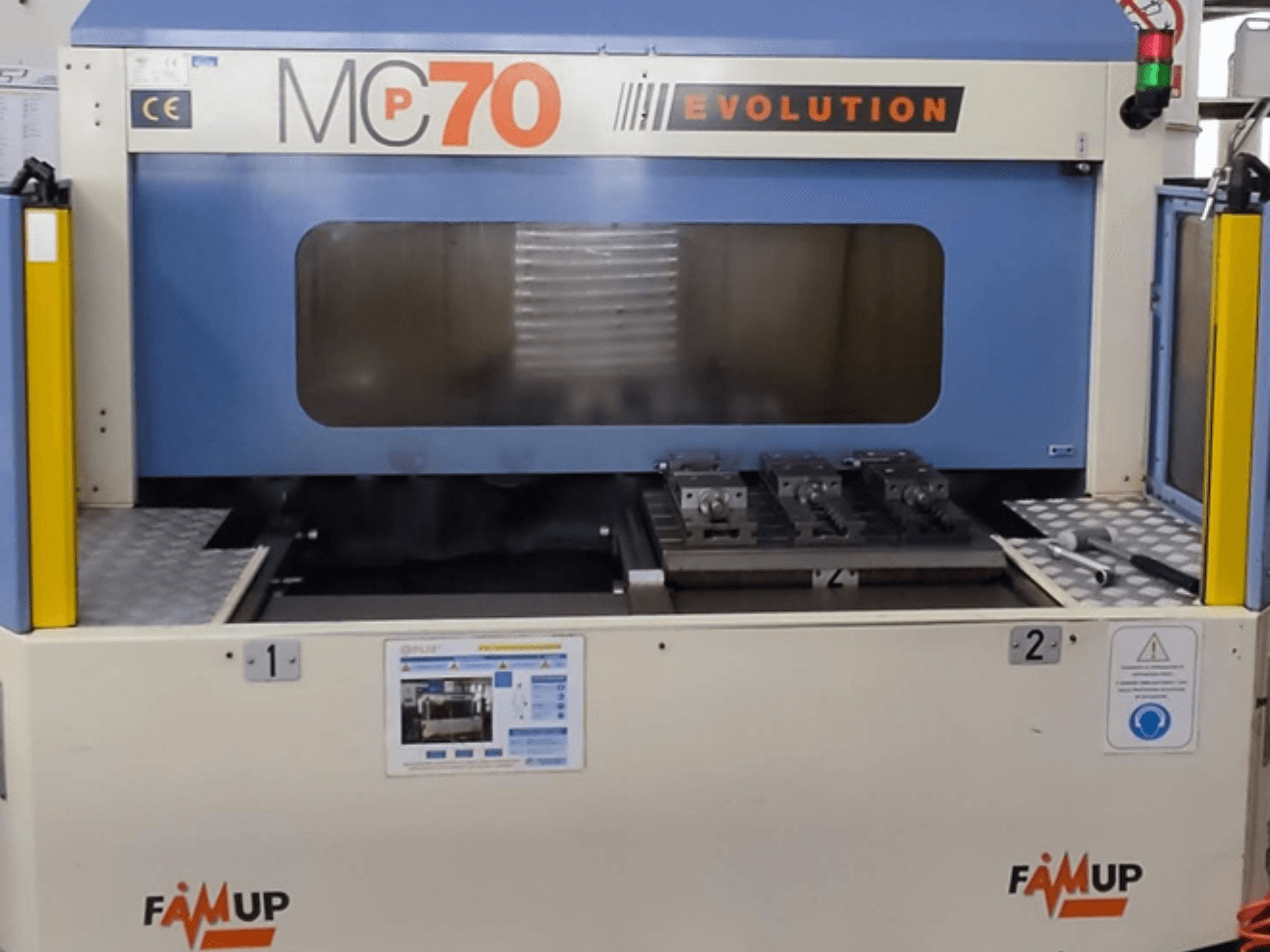 Centro di lavoro verticale FAMUP MCP70 E, vista frontale che mostra il pannello di controllo e l'area di lavoro con attrezzature e dispositivi di sicurezza.