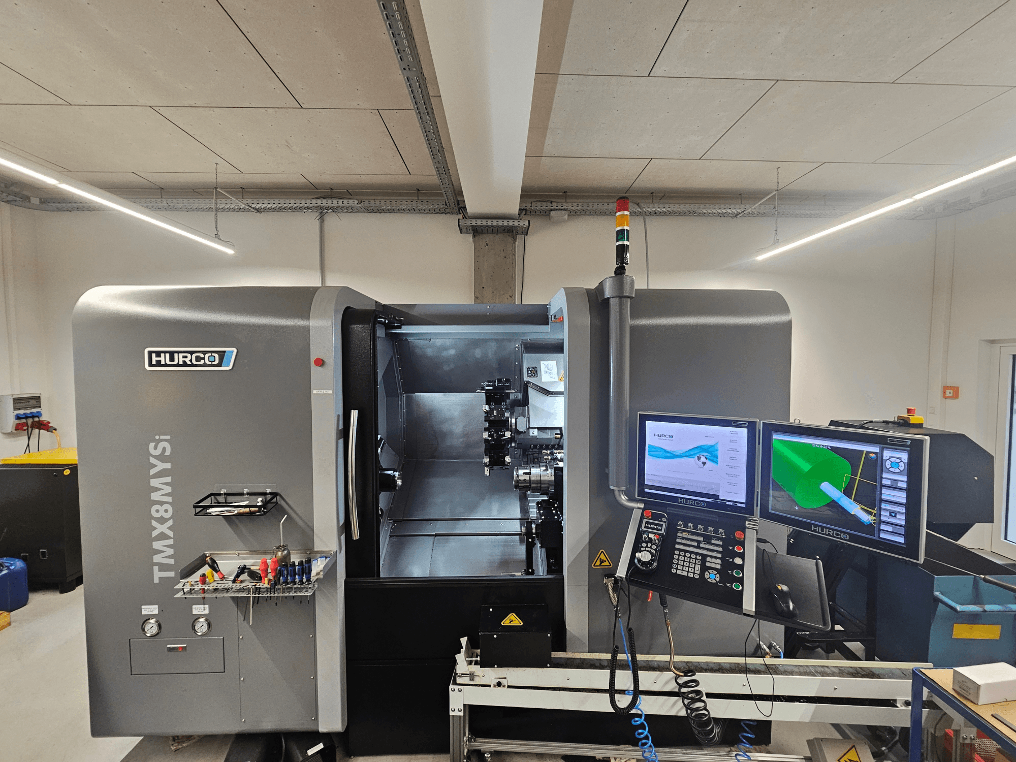 Centro di tornitura Hurco TMX 8 MYSi in un'officina, con doppio monitor, pannello di controllo e utensili laterali.
