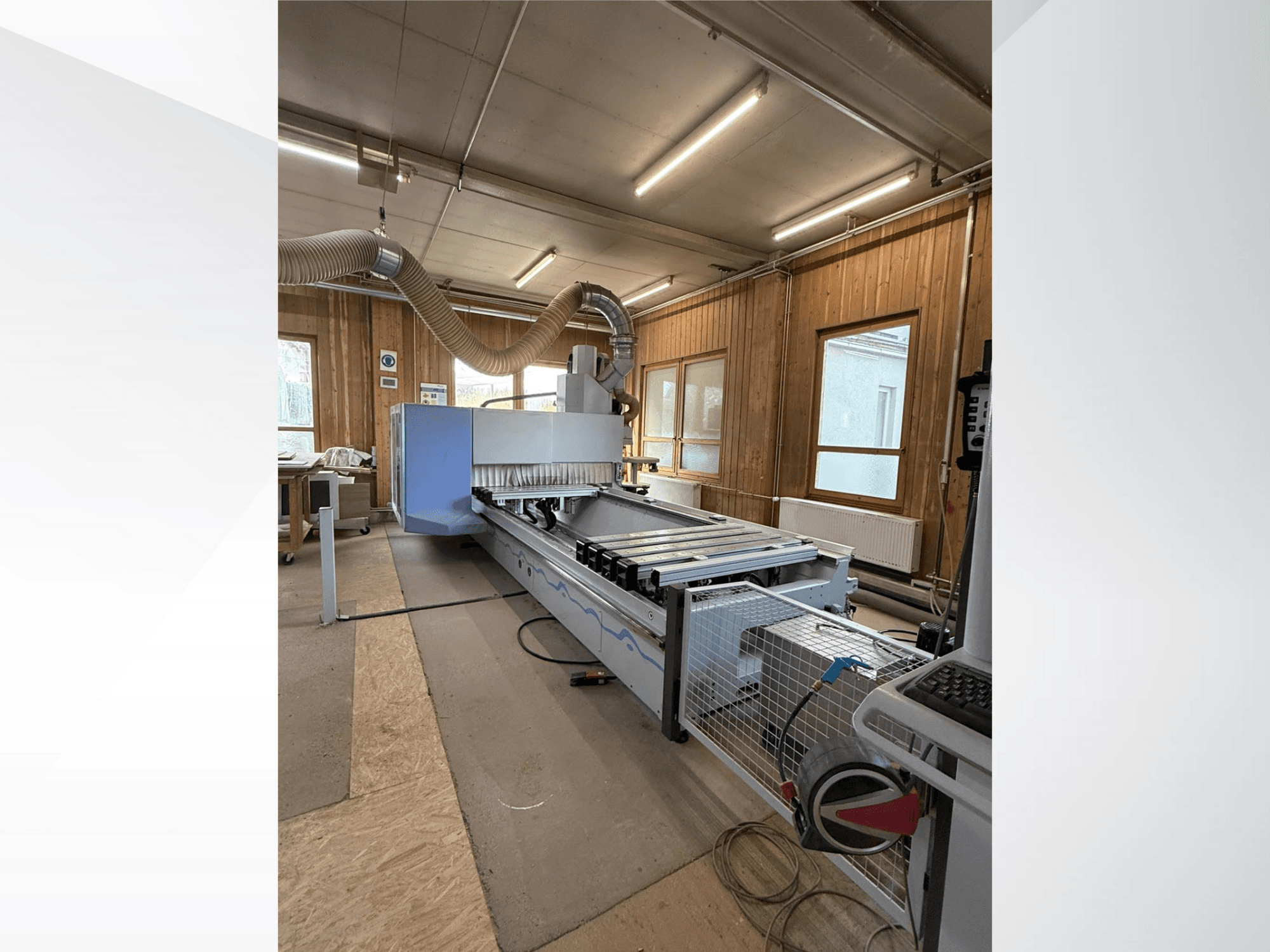 Fresatrice CNC in un'officina, vista laterale, con un grande corpo blu, un nastro trasportatore collegato e un pannello di controllo visibile.