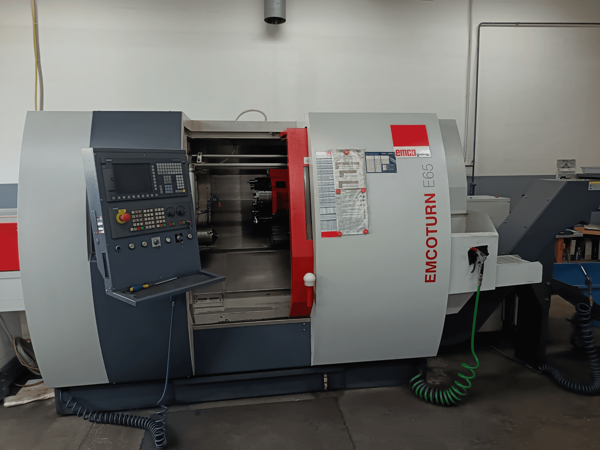 Centro di tornitura EMCO EMCOTURN E65, vista frontale che mostra il pannello di controllo, il meccanismo interno e le caratteristiche in un'officina.