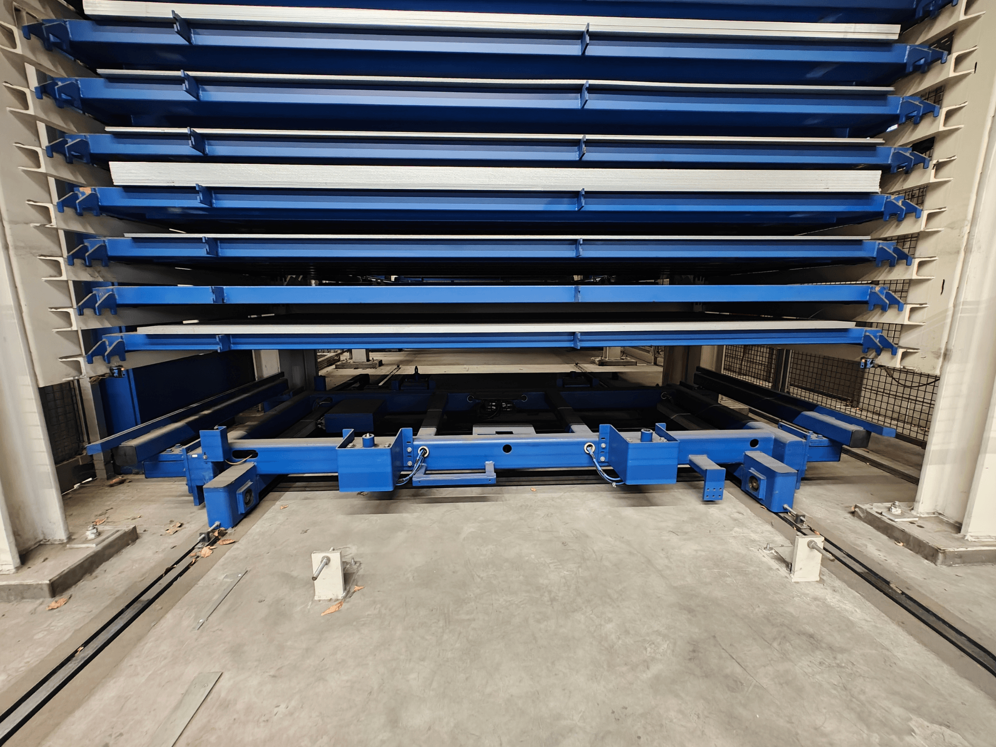 Scaffale industriale blu con più ripiani orizzontali, visto dal davanti. Dispone di un meccanismo di sollevamento e di travi di sostegno.