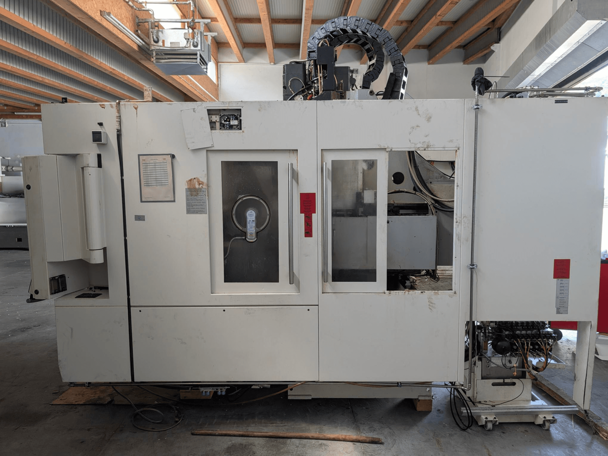 Centro di lavoro verticale STAMA MC 326, vista laterale che mostra il pannello di controllo, l'area del mandrino e varie etichette sulla macchina.