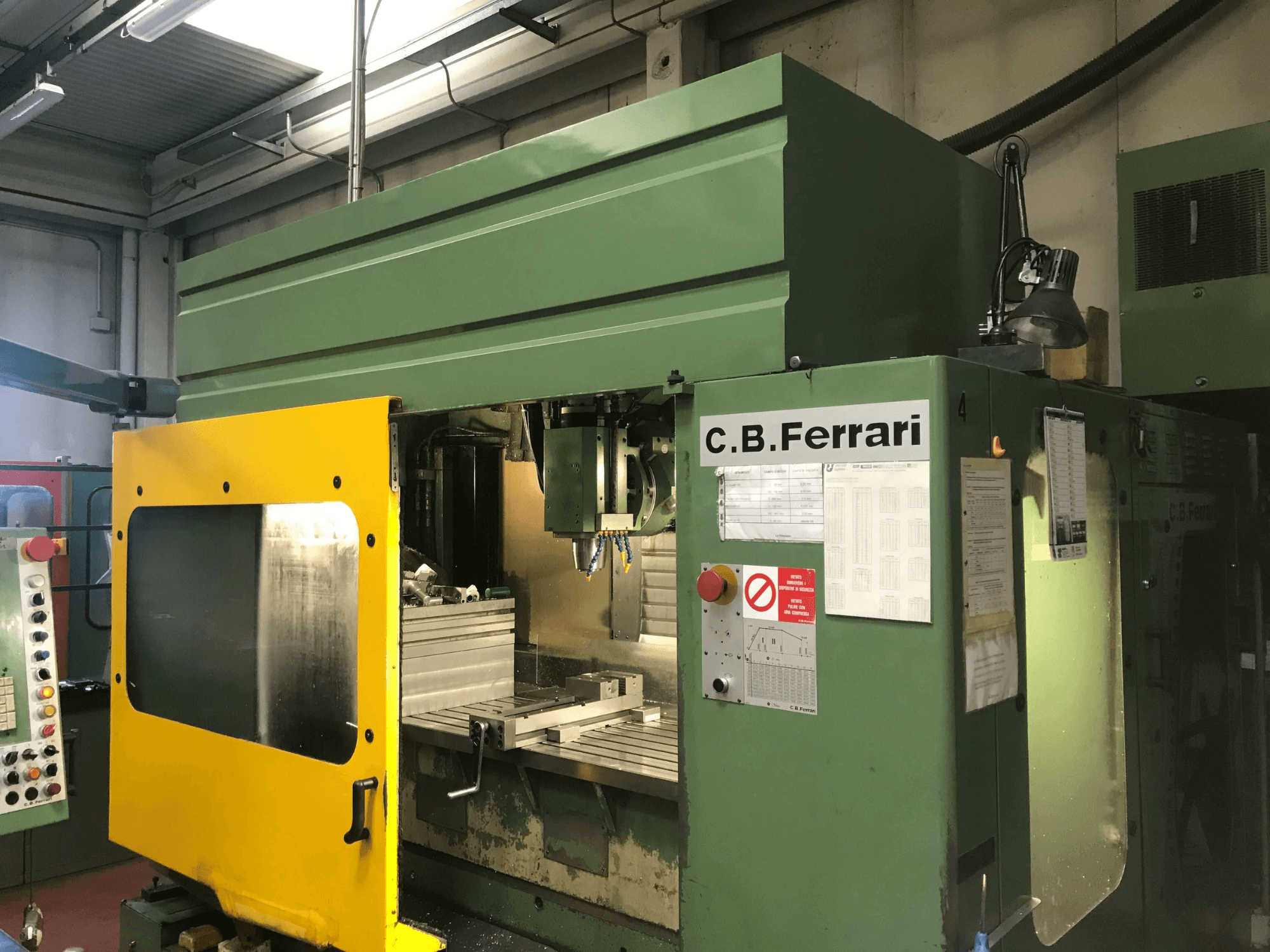 Centro di lavorazione verticale C.B. Ferrari B16, vista frontale con porta di sicurezza gialla, pannello di controllo e area di lavorazione visibili.