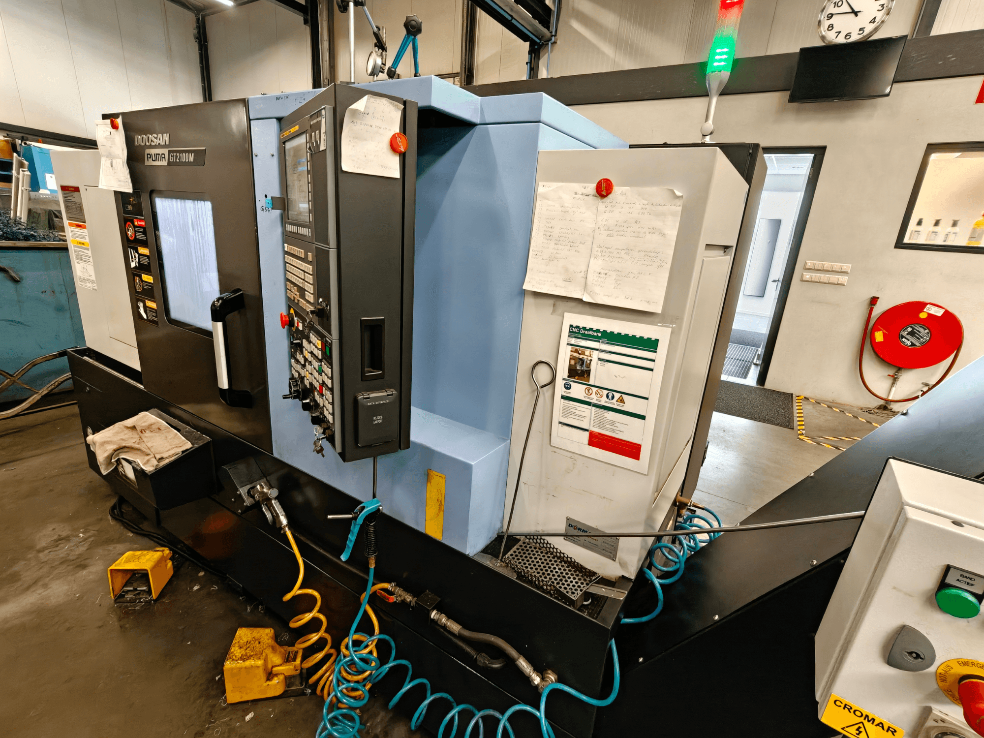 Vista frontale del tornio orizzontale DOOSAN Puma GT 2100M con pannello di controllo, caratteristiche di sicurezza e note di manutenzione visibili.