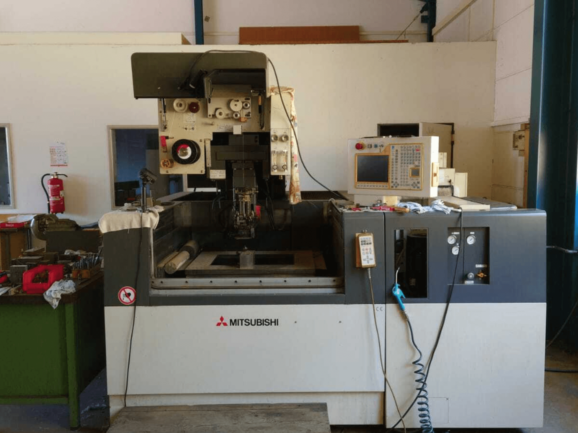 Vista frontale della macchina per elettroerosione a filo Mitsubishi FA20, con pannello di controllo, area di lavoro e segnaletica di sicurezza visibili.