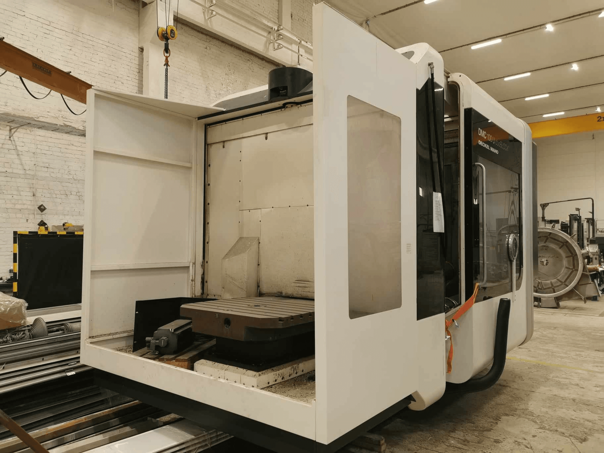 Macchina CNC lineare DMC 100U, vista laterale con porta di accesso aperta, che mostra il piano di lavoro e i componenti interni.