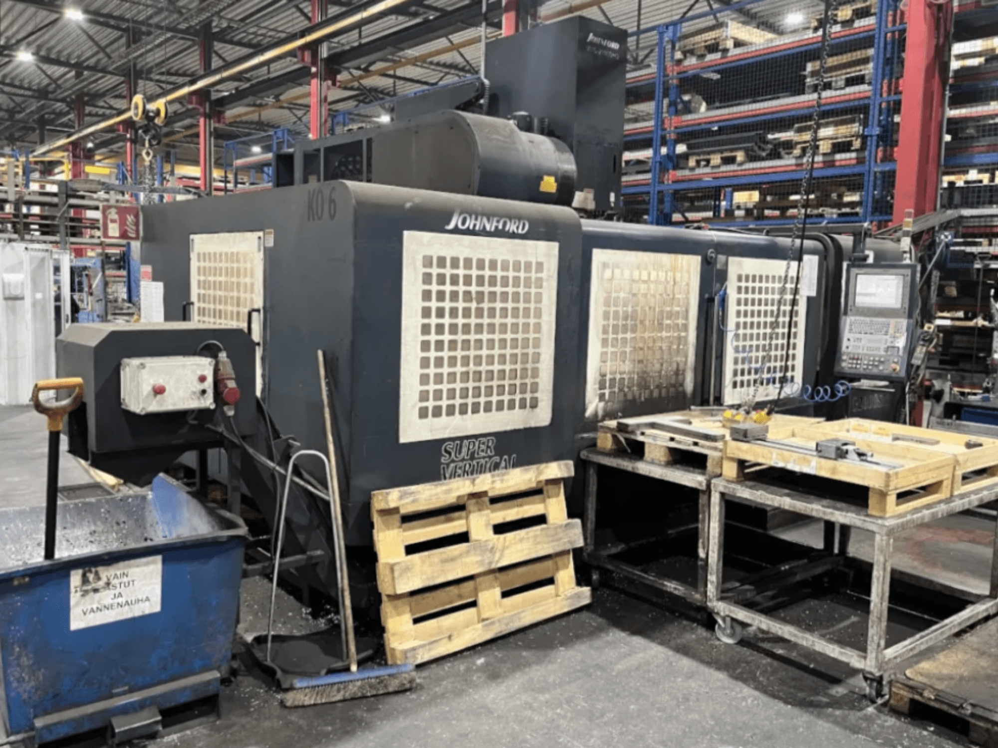 Fresatrice Super Vertical Johnford in uno stabilimento, vista laterale con pannello di controllo, pallet e attrezzature di pulizia nelle vicinanze.