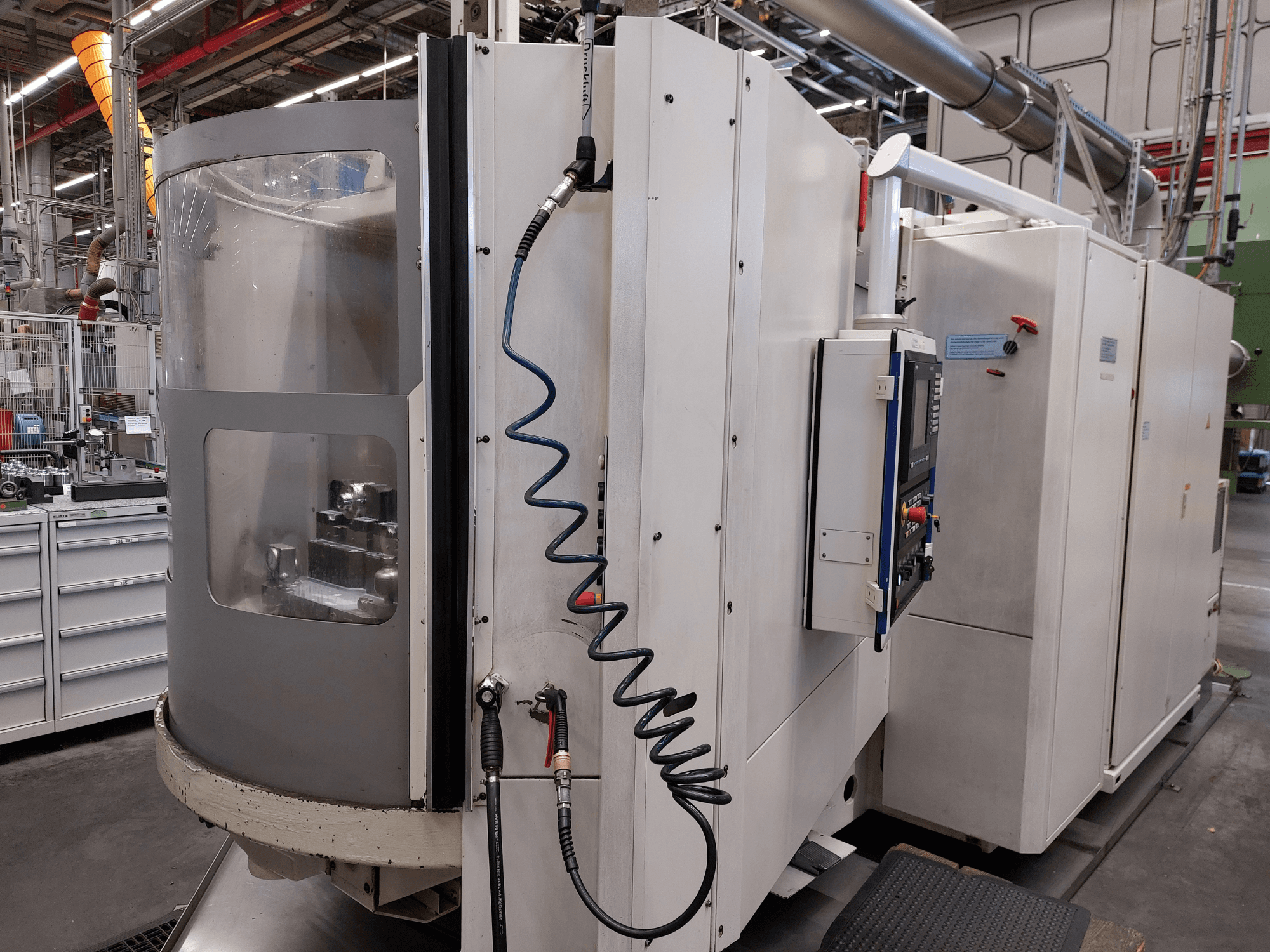 Centro di lavorazione orizzontale Heller MC 16 visto di profilo, con in primo piano il pannello di controllo, il tubo dell'aria e la finestra trasparente che offre una vista dell'area di lavoro.