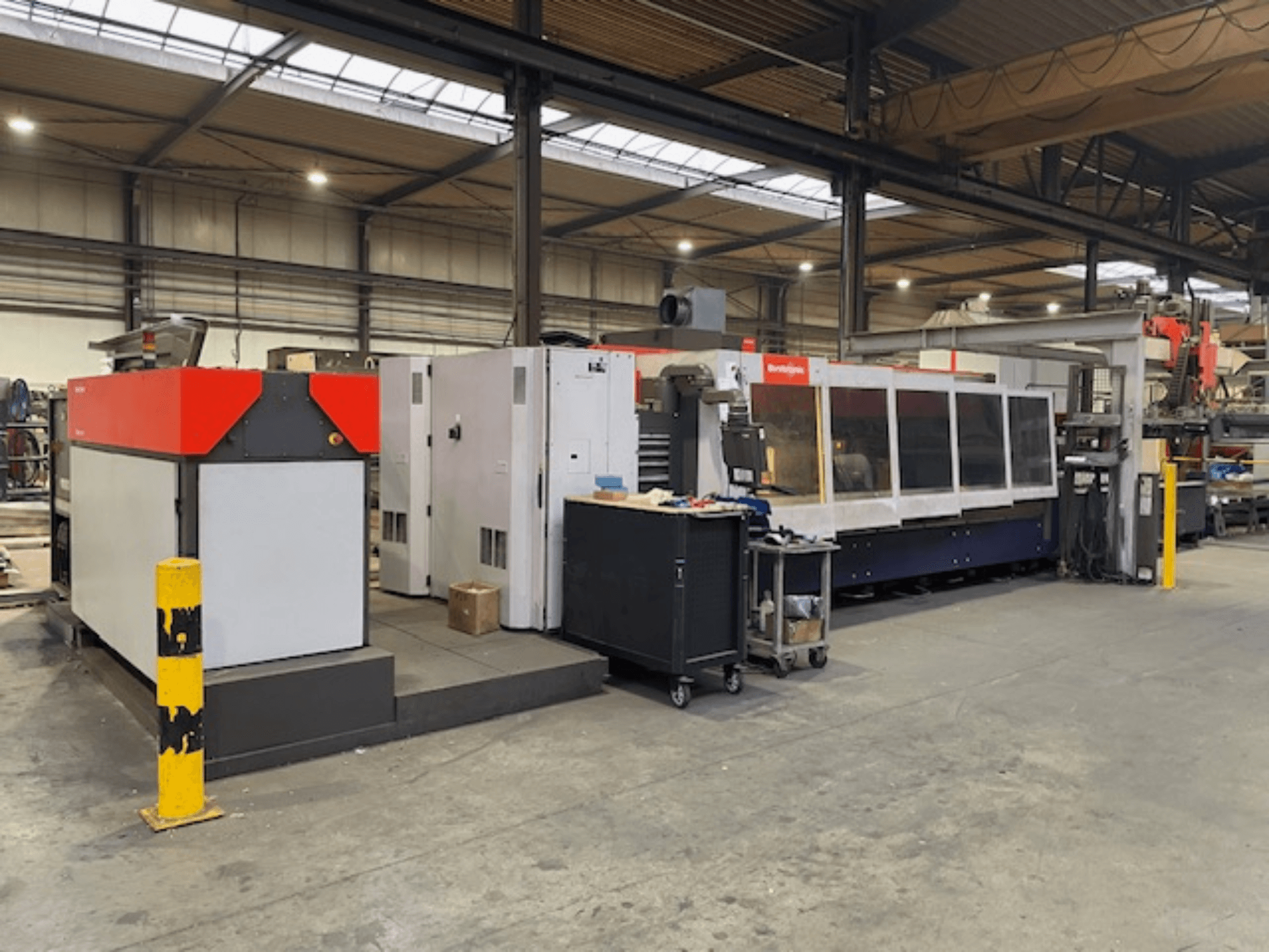 Macchina di taglio laser Bystronic BySpeed 3015 CO2, vista laterale in un'officina, con elementi di design distinti in rosso e grigio.