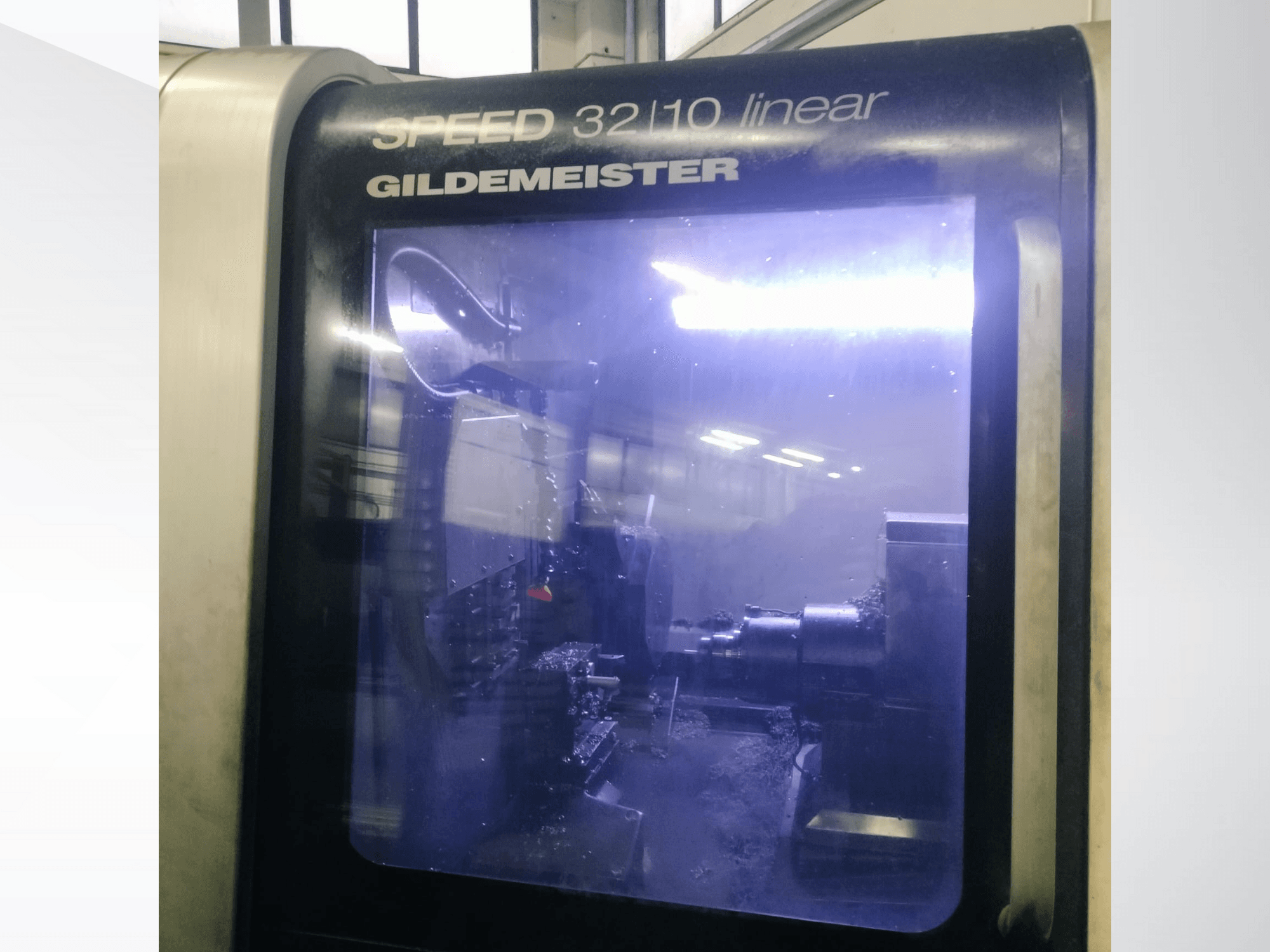 Vista frontale della macchina CNC lineare Gildemeister SPEED 3210, che mostra i componenti interni e il refrigerante liquido in funzione.