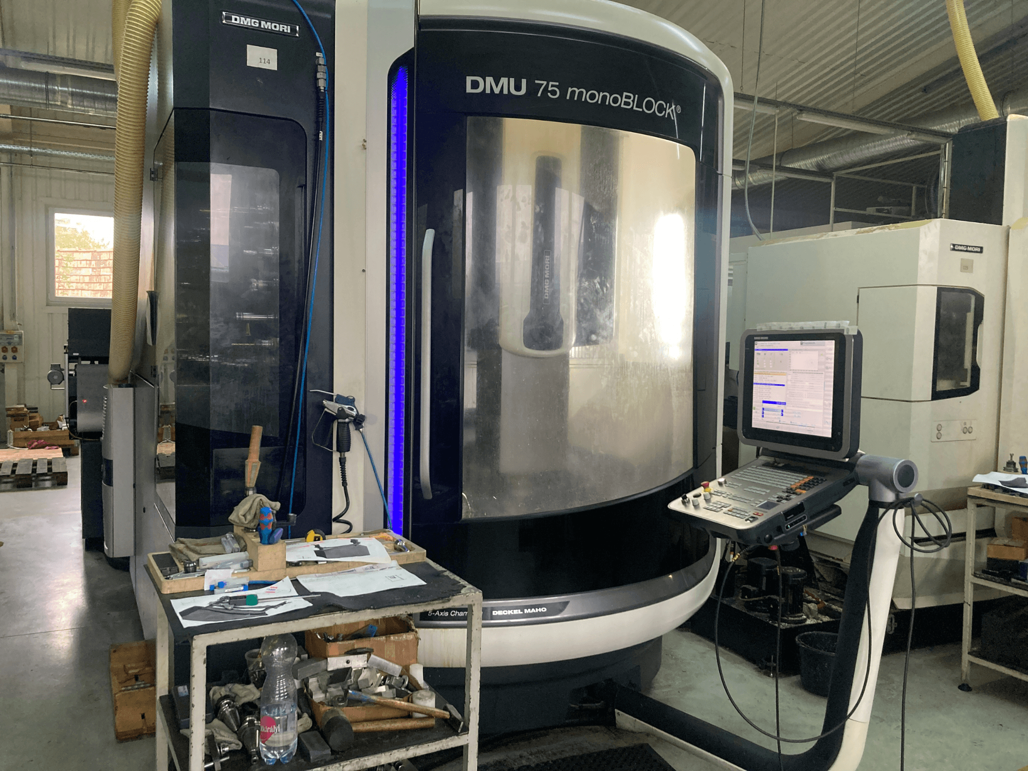 Macchina DMG MORI DMU 75 monoBLOCK® CNC, vista frontale, con pannello di controllo, utensili e area di lavoro con materiali.