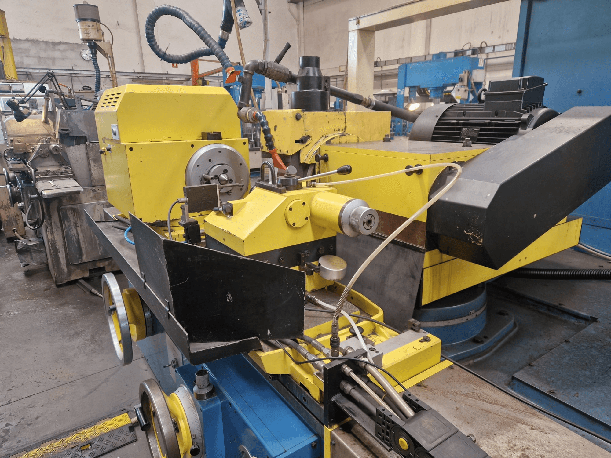 Macchina industriale gialla con sezione nera, con quadrante e tubi flessibili, vista frontalmente con una leggera angolazione.